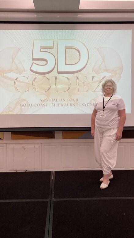 A person standing next to a presentation screen displaying "5D CODEZ Australian Tour Gold Coast Melbourne Sydney." Rhonda from Regain Esteem wears a white outfit and a name badge.