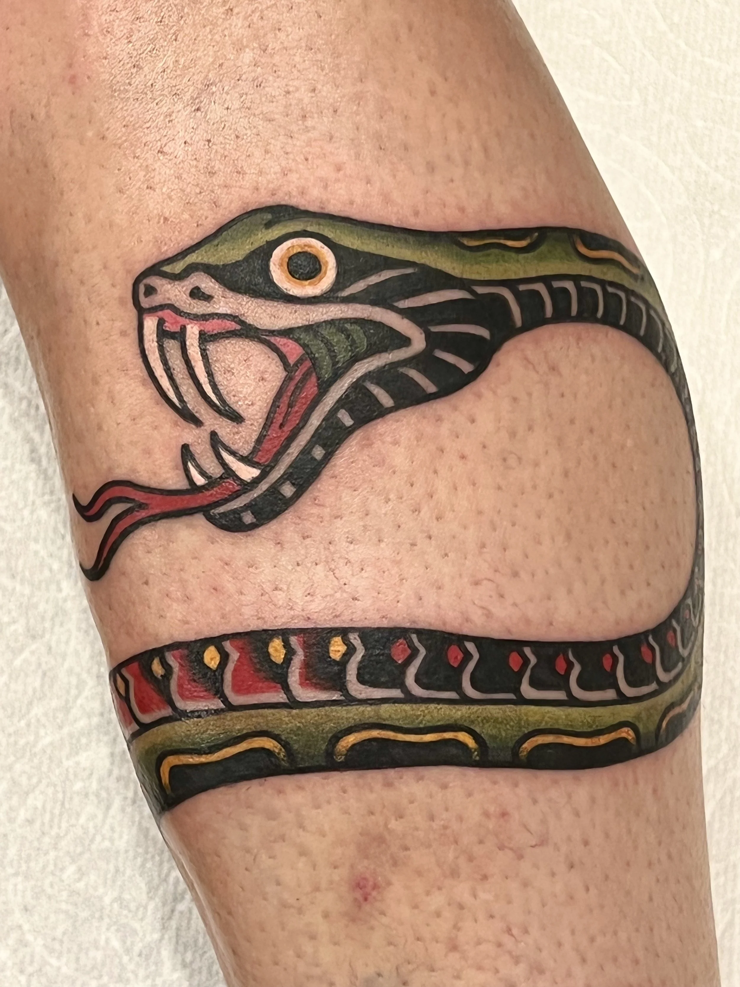 A colorful traditional tattoo of a snake's head and body on a person's lower leg.