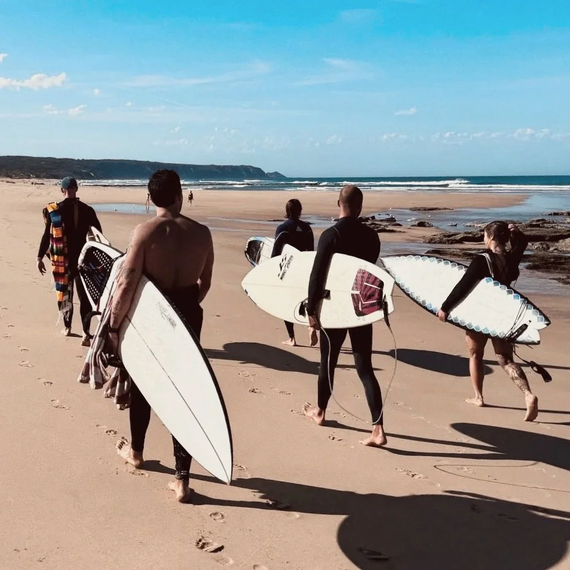 Group of surfers carrying surfboards on the beach towards the ocean in Australia.