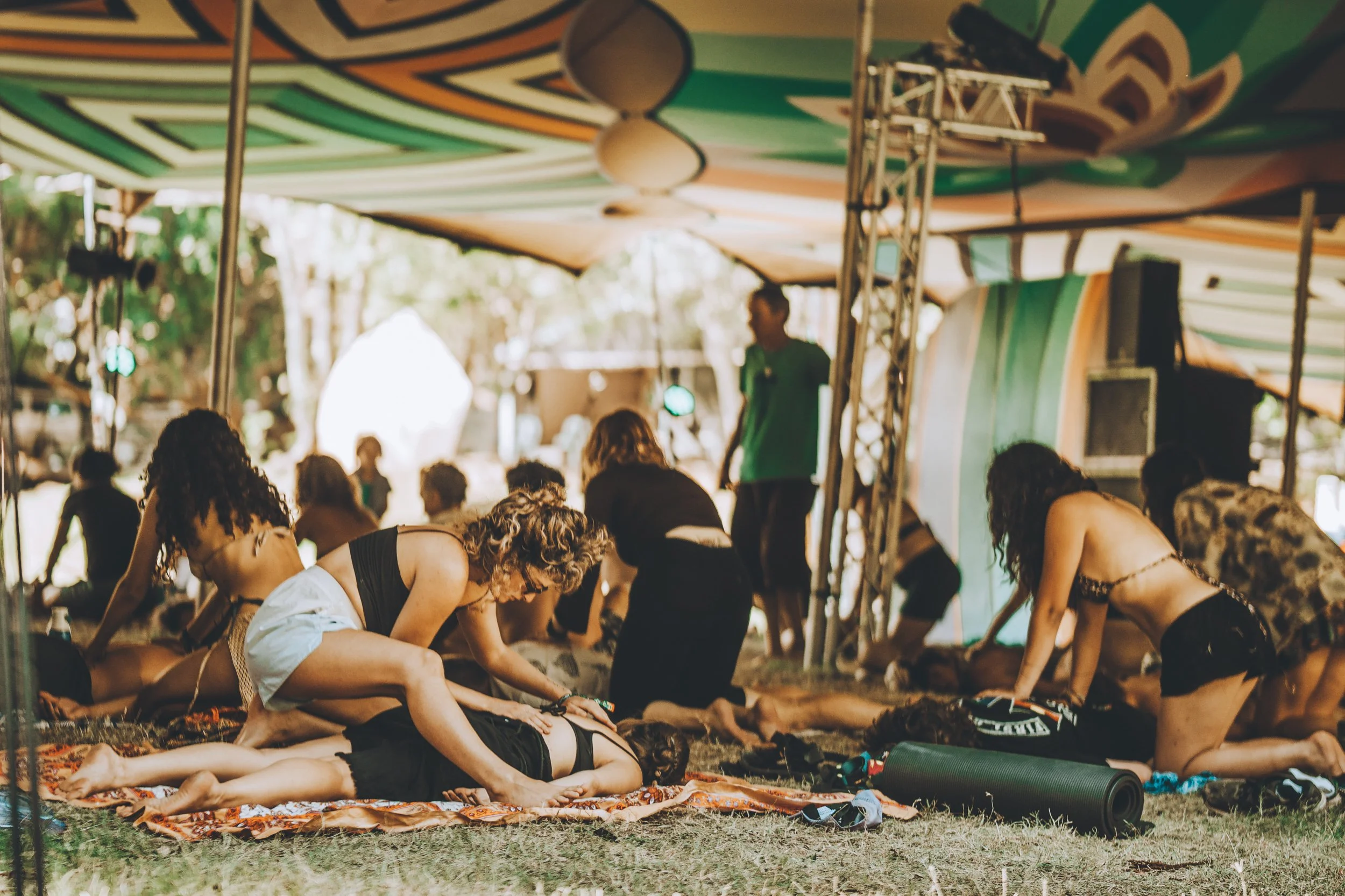 People practicing yoga outdoors under a colorful tent.