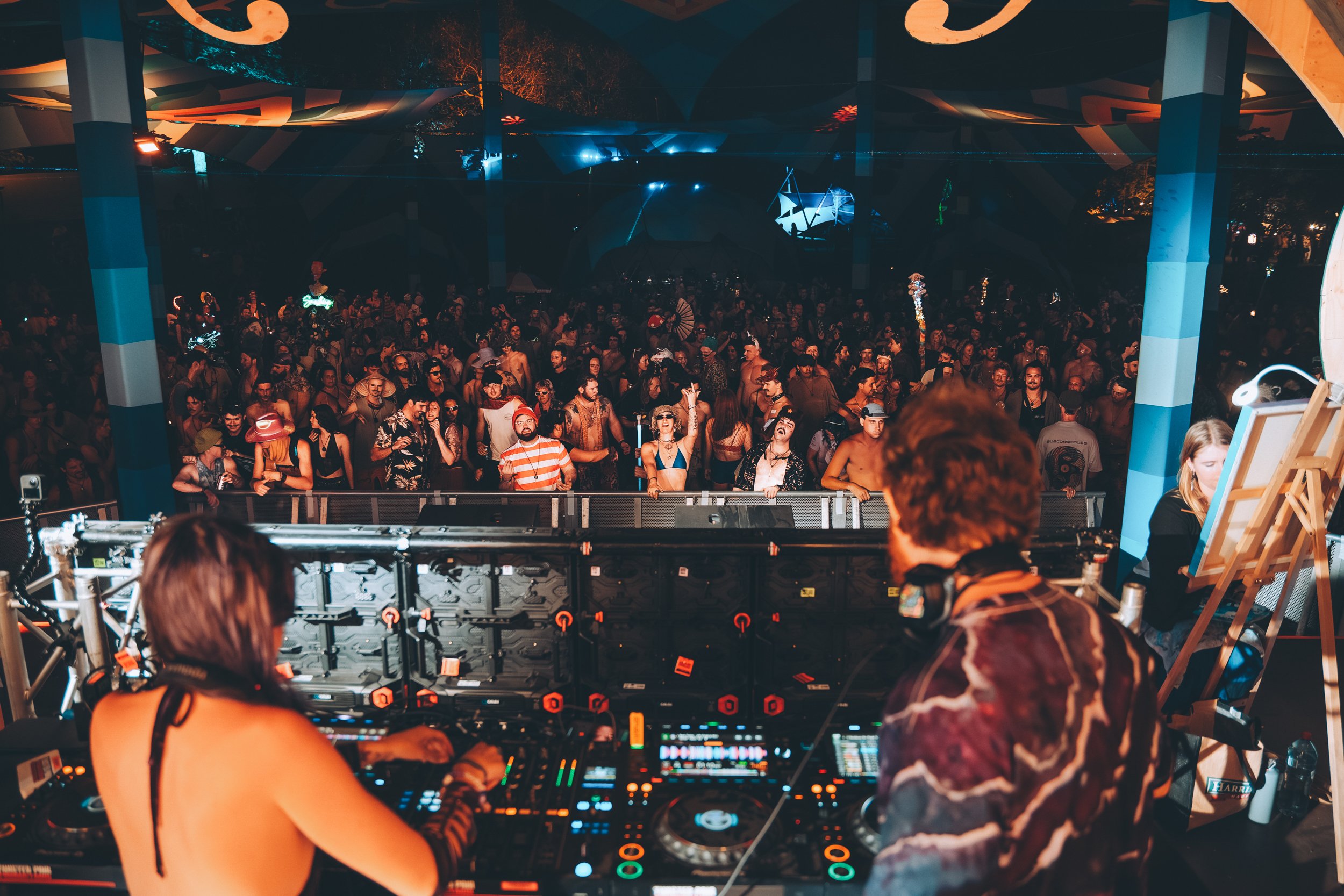 DJ performing at a music festival with a large crowd dancing in front at night.