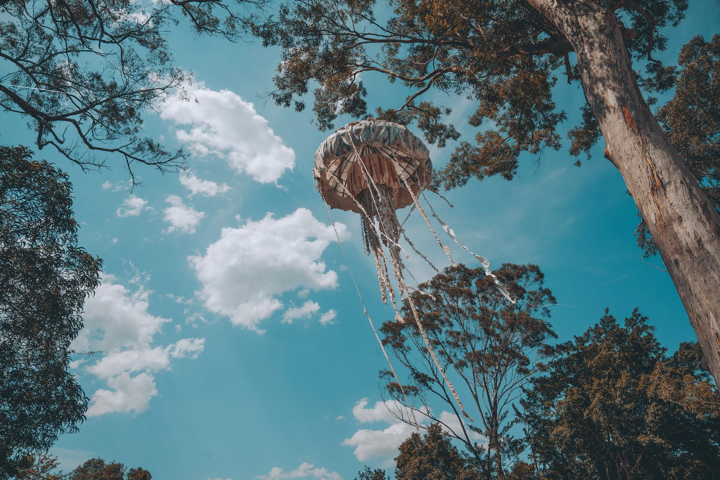 A flying jellyfish-shaped hot air balloon in the sky, surrounded by trees and clouds.