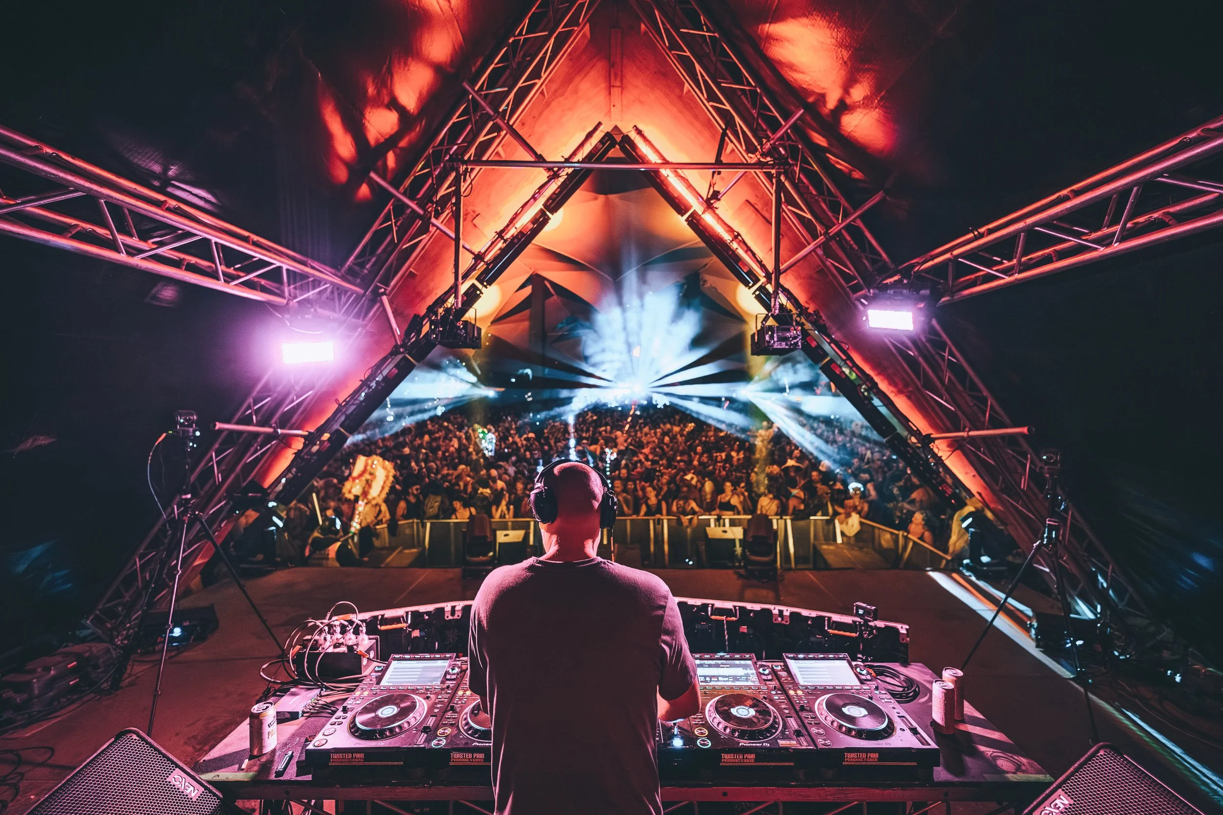 DJ performing at a colorful concert with a stage, lighting effects, and a crowded audience.