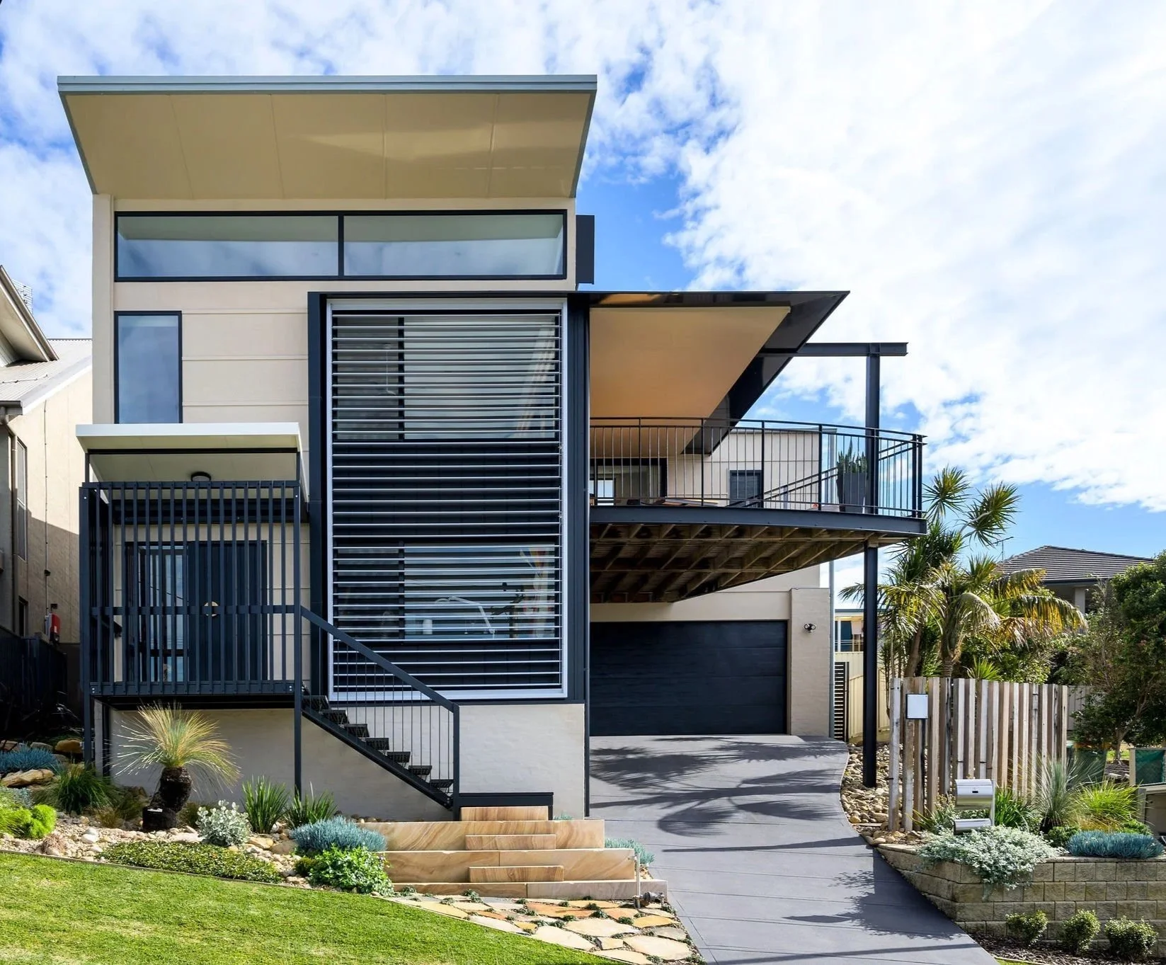 Exterior of modern building with metal slatted facade, large window, staircase, and landscaped small garden.