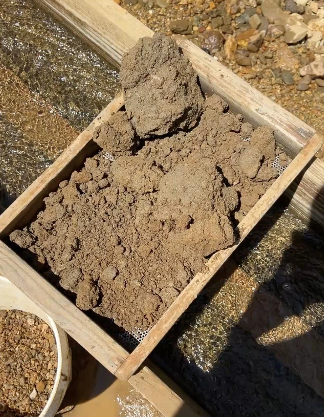 Add in the dirt.  Breaking down the clumps can be difficult.  Don’t be shy to push against the screen in the water to help get it moving.  Corundum is much harder than the metal screen, so you won’t scratch up your finds.