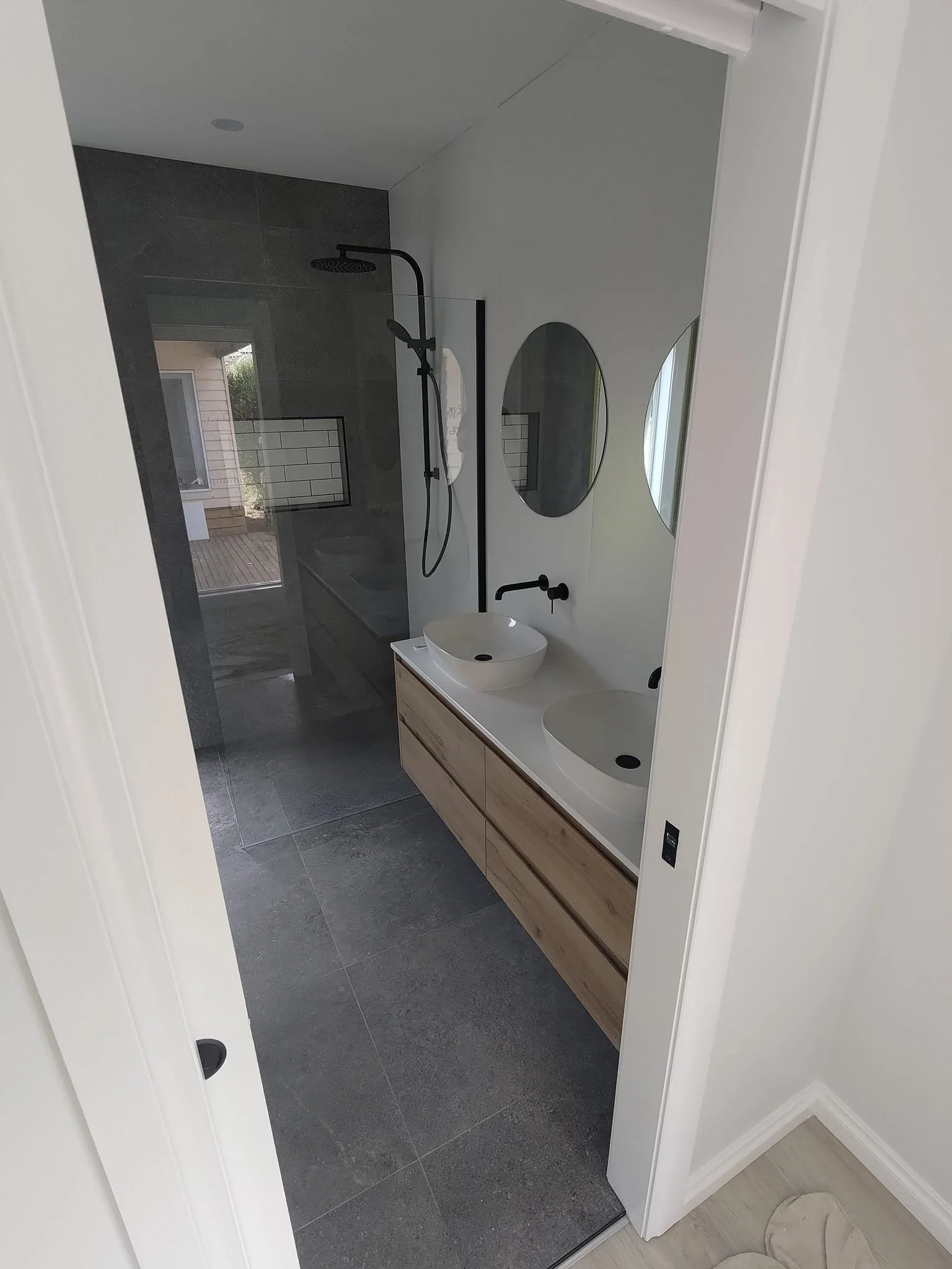 Modern bathroom with dual sinks, round mirrors, and a rain showerhead in a walk-in shower.