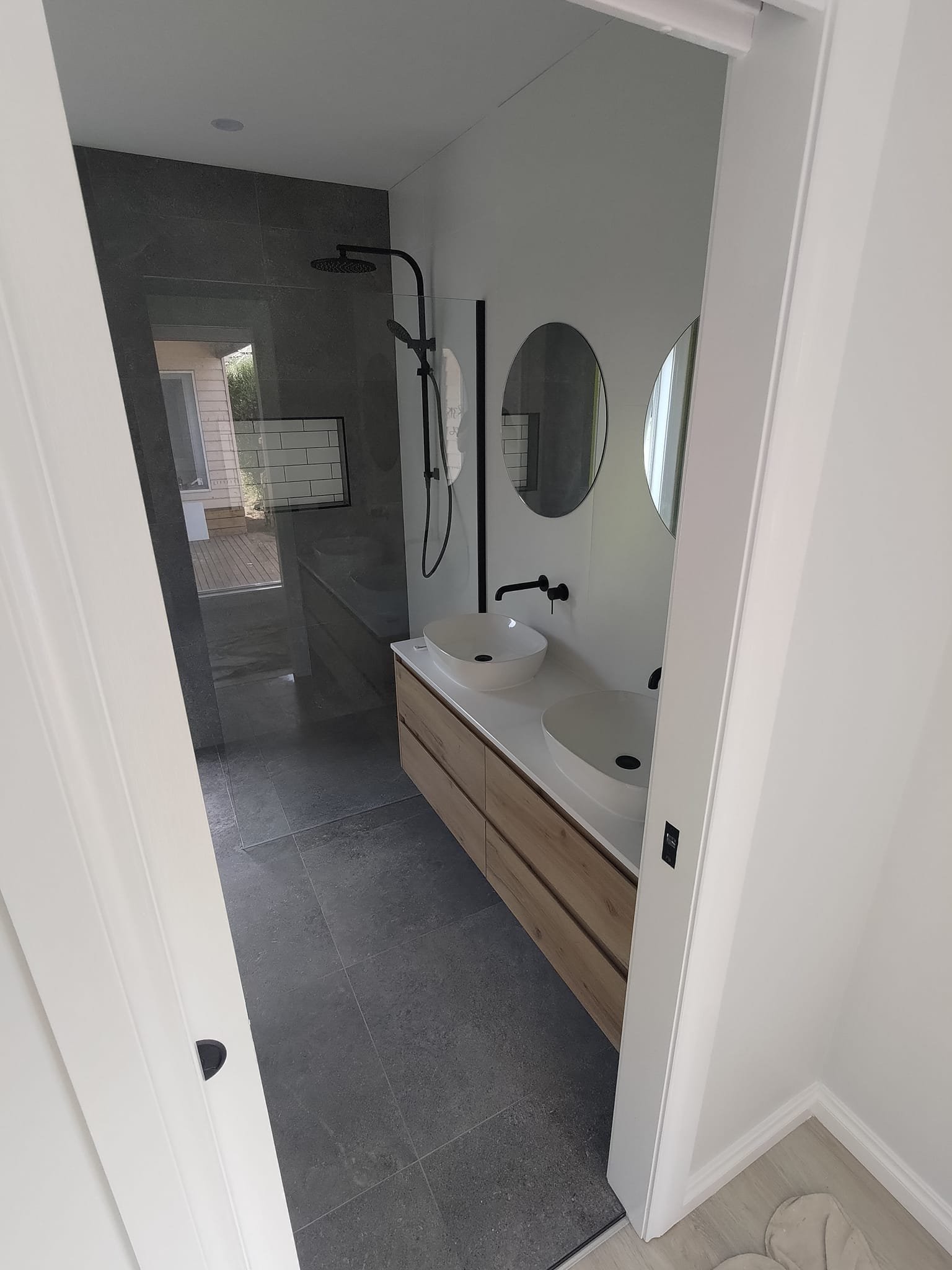 Modern bathroom with double sinks, round mirrors, and a walk-in shower with a black showerhead.