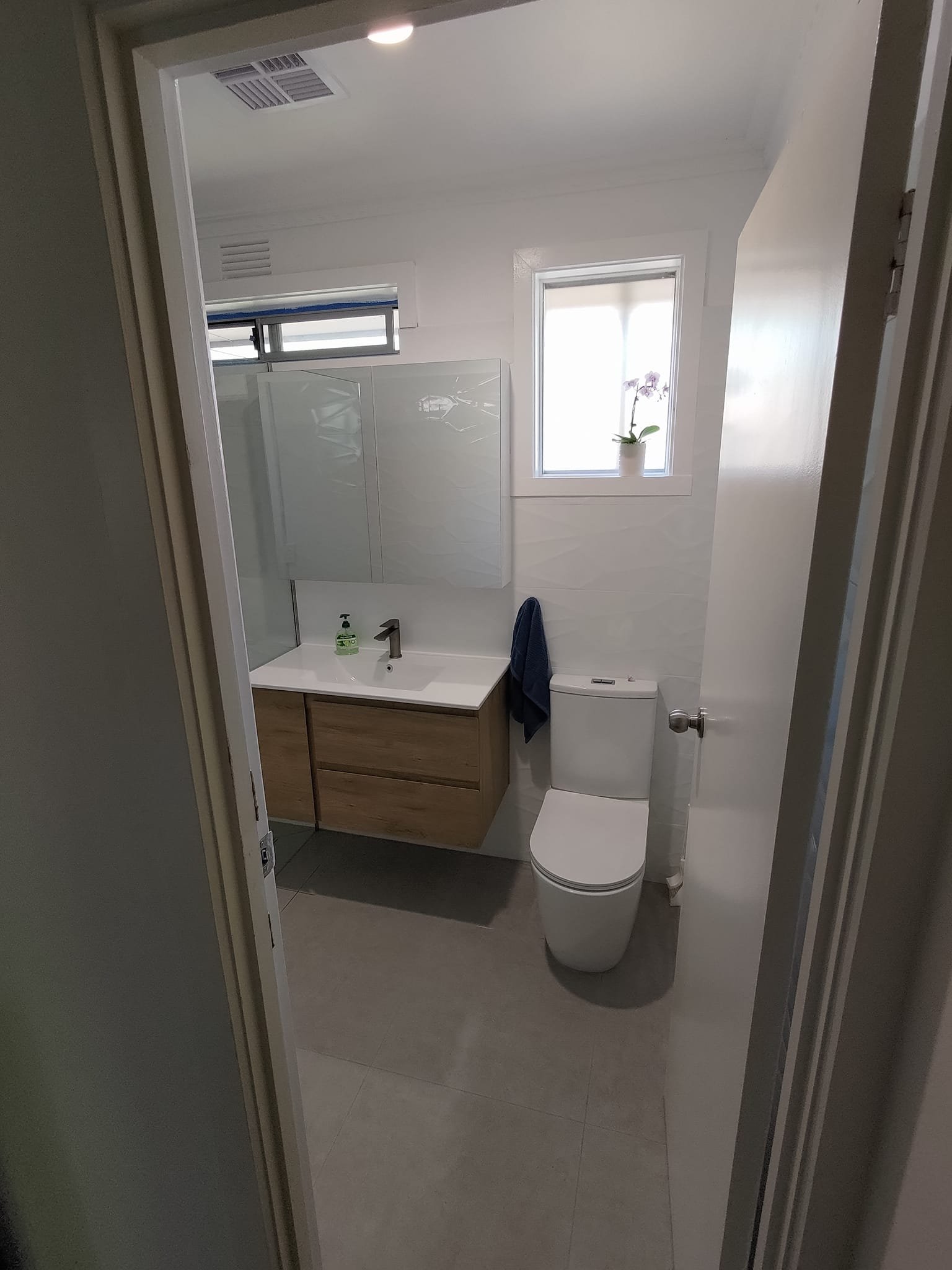 Modern bathroom interior with a toilet, wall-mounted sink, wooden cabinet, towel, and a small window with potted plant.
