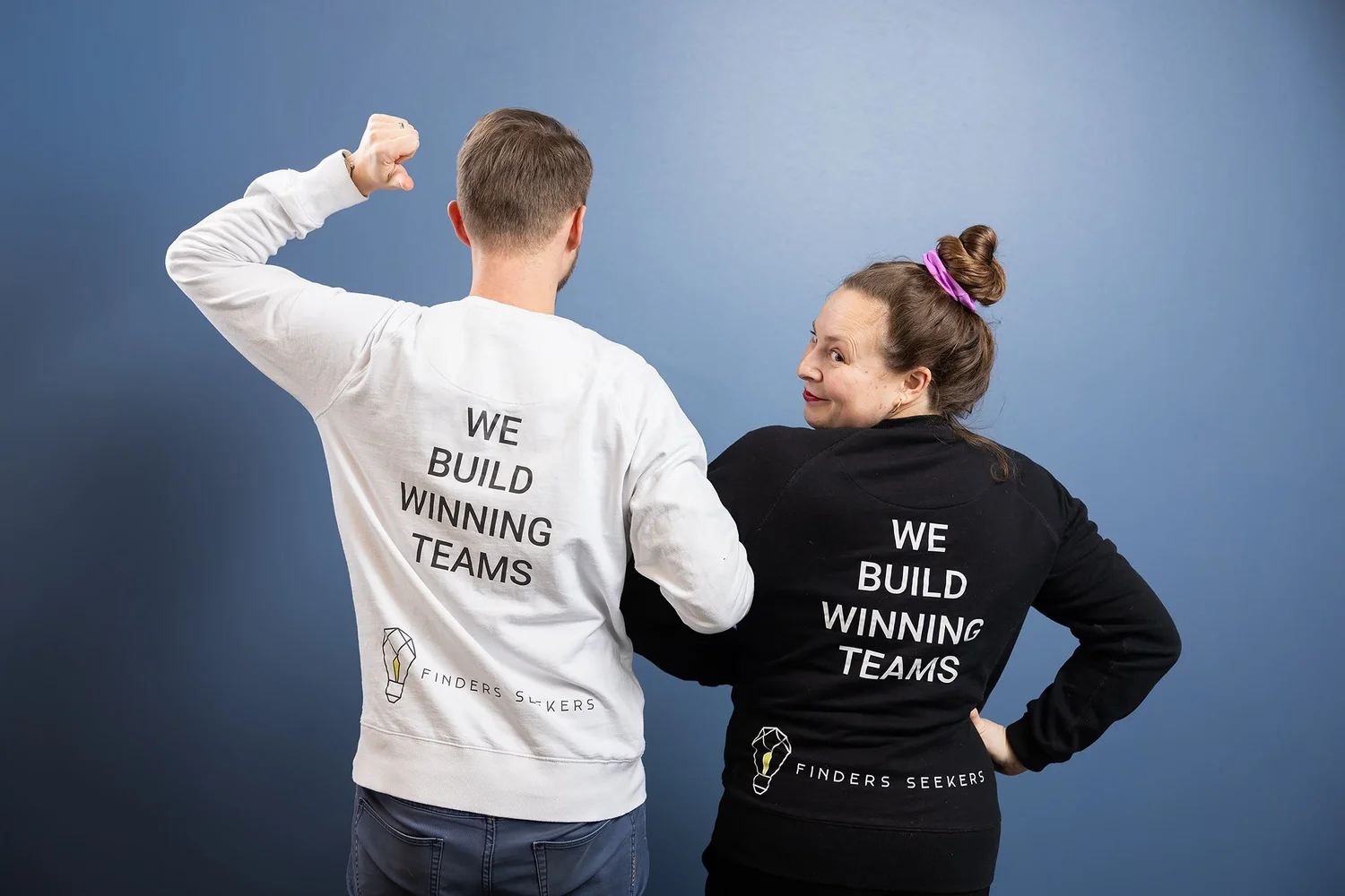 Two team members flexing in sweatshirts printed We Build Winning Teams