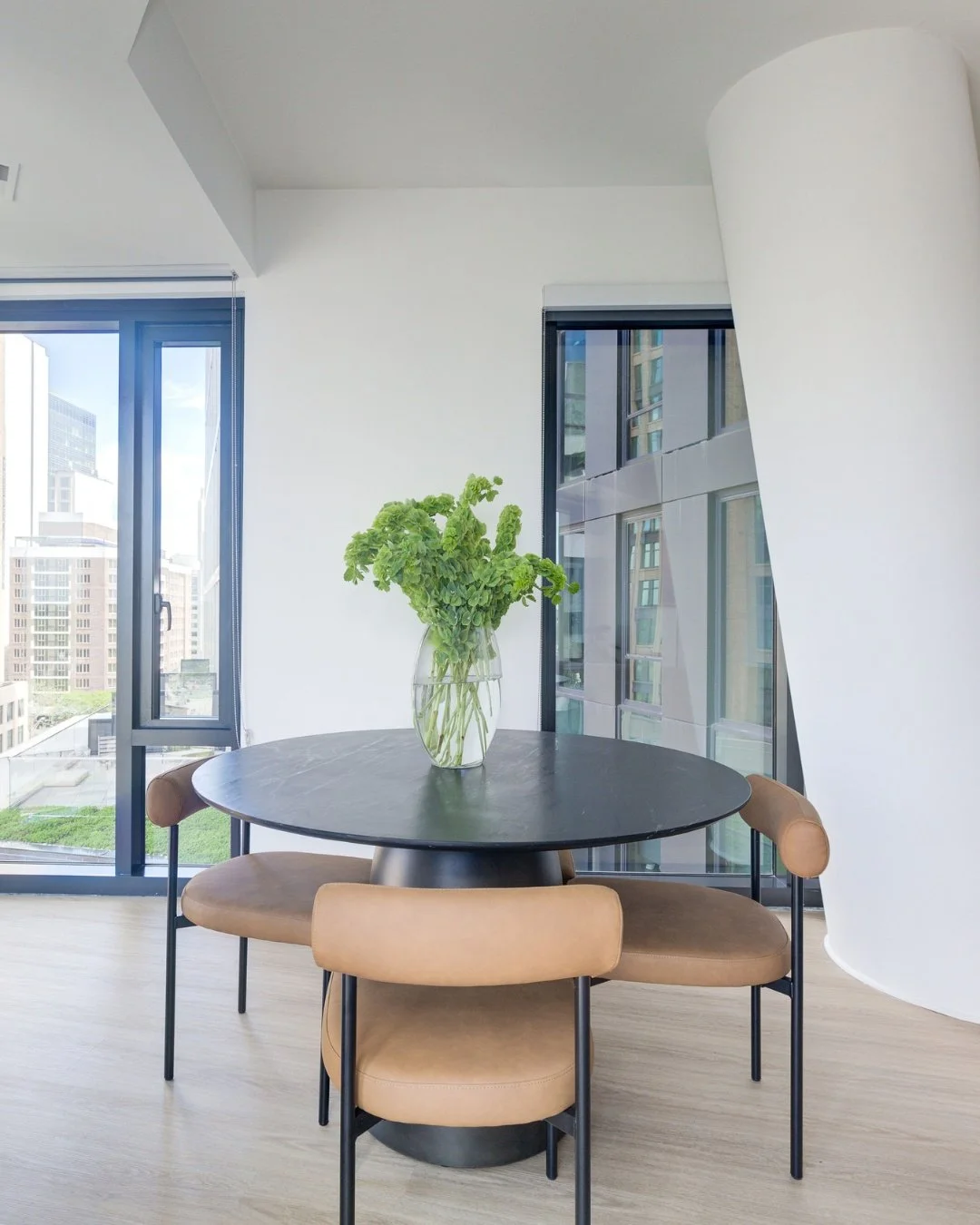 A round table in a small dining nook solves more problems than people expect.

It seats comfortably without corners eating into circulation. In a room with this much natural light coming through the black-framed windows, it does not compete with the 