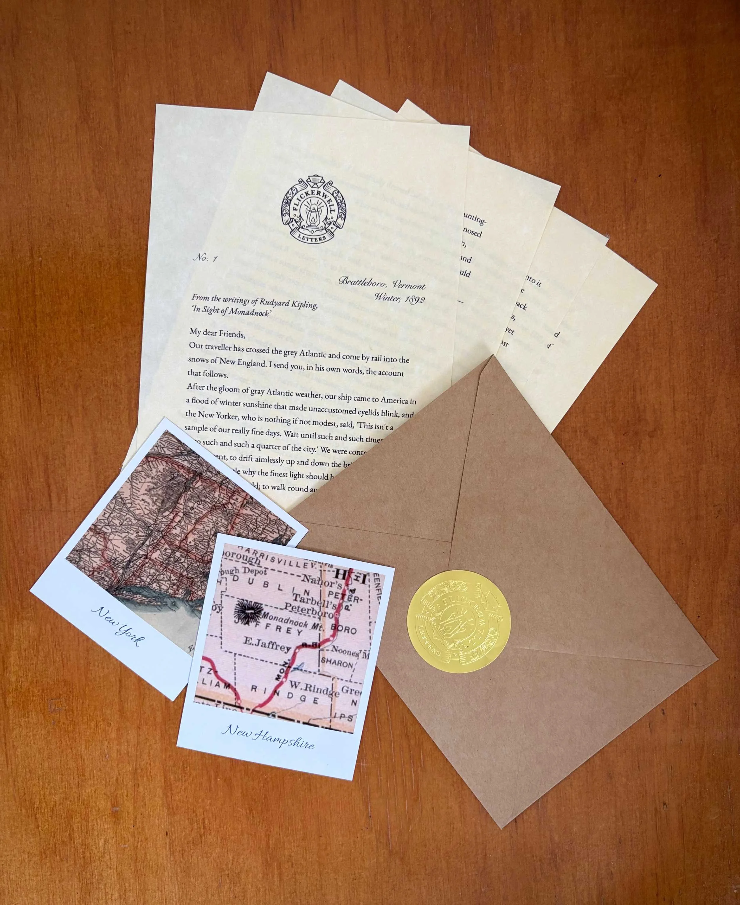 Four pages of the first Flickerwell Letters dispatch, fanned out on a wooden table alongside two Polaroid-style prints of historic maps, and an envelope sealed with an embossed Flickerwell Letters stamp.