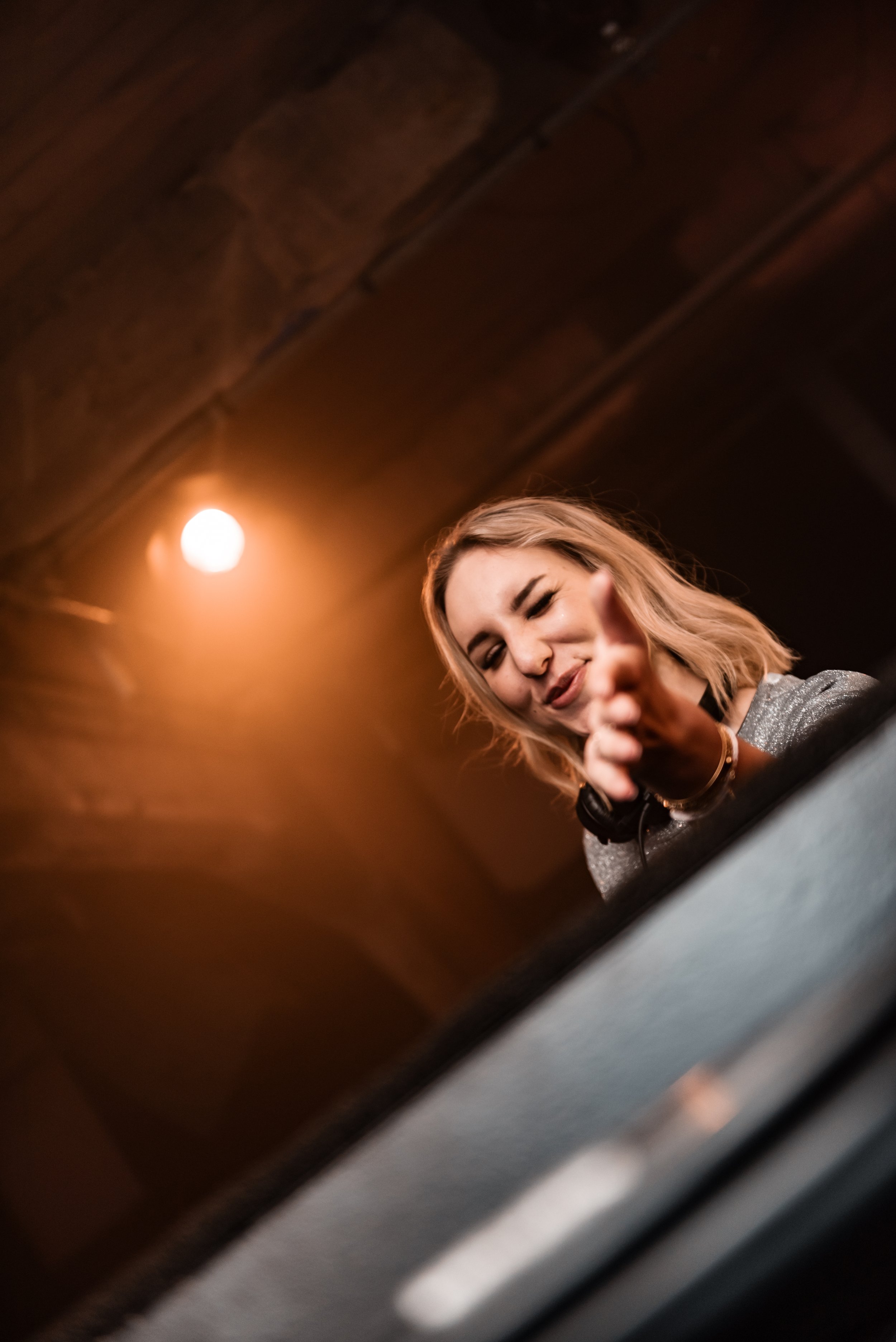 DJ performing at a nightclub, reaching out with hand, warm lighting, headphones around neck.