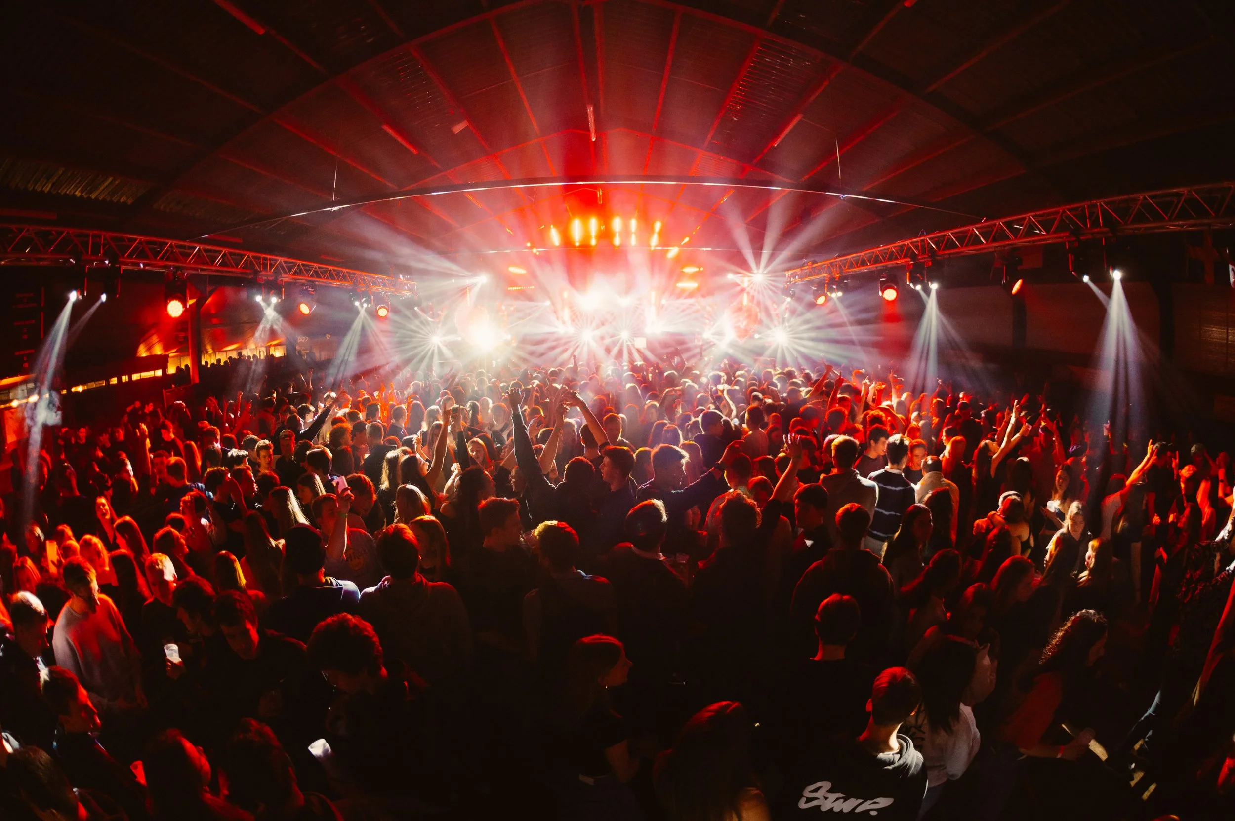 Crowded concert with bright stage lights and red ambient lighting.