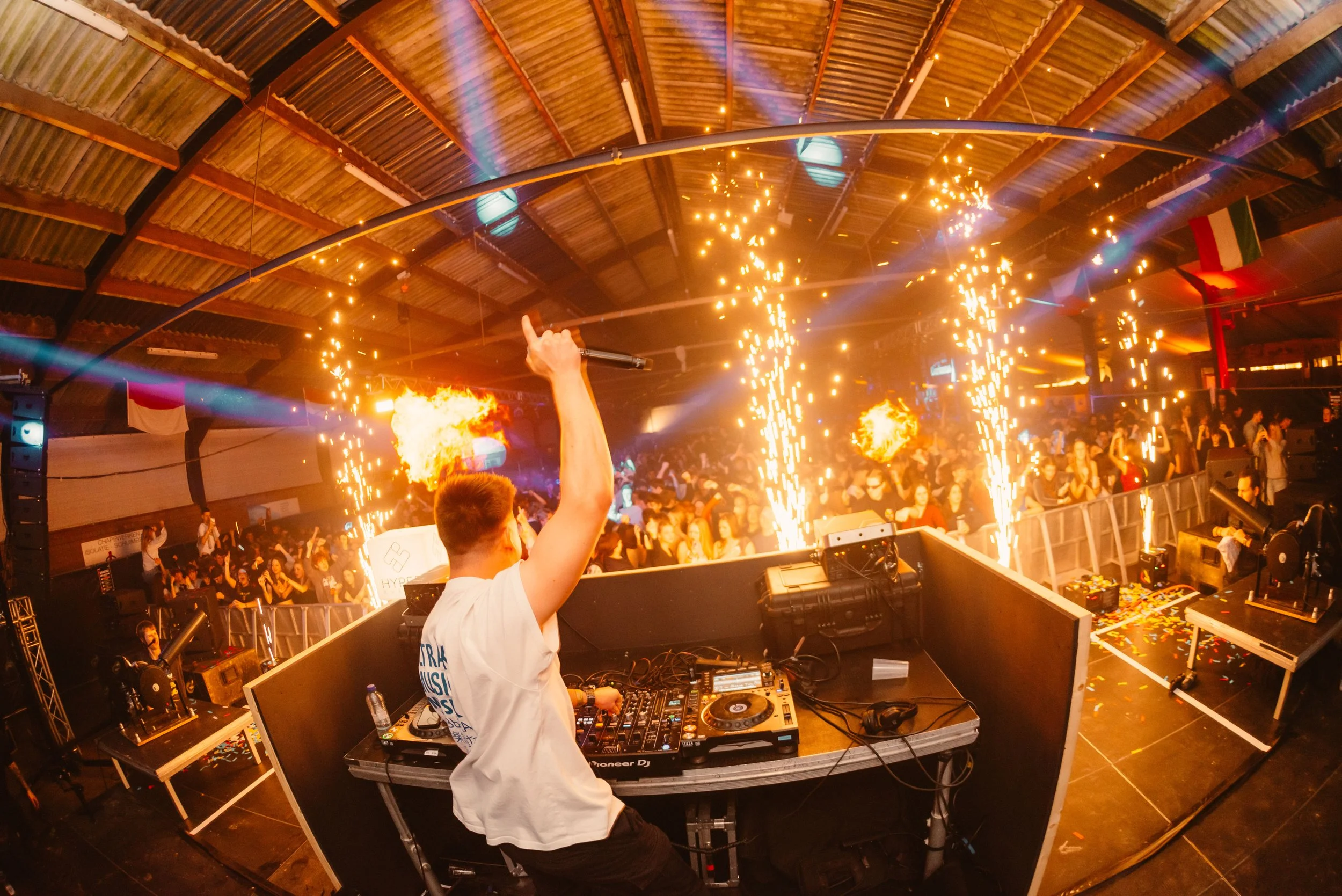 DJ performing on stage with fireworks and crowd at a music event.