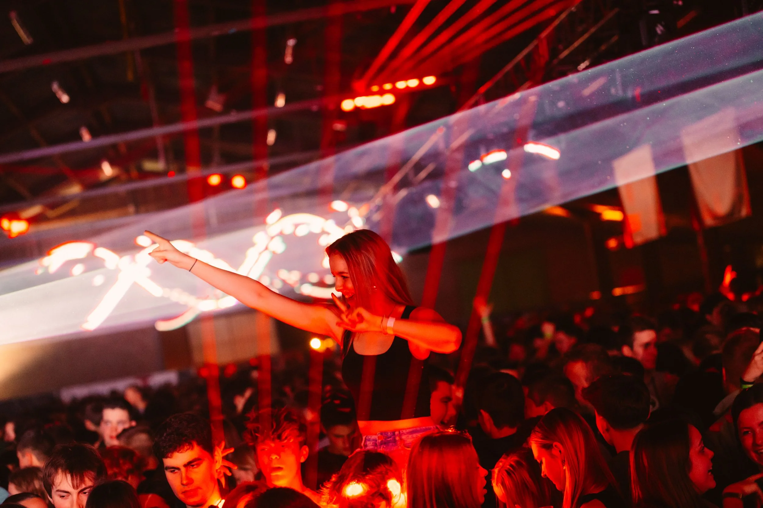 People dancing at a crowded nightclub with red lights and lasers.