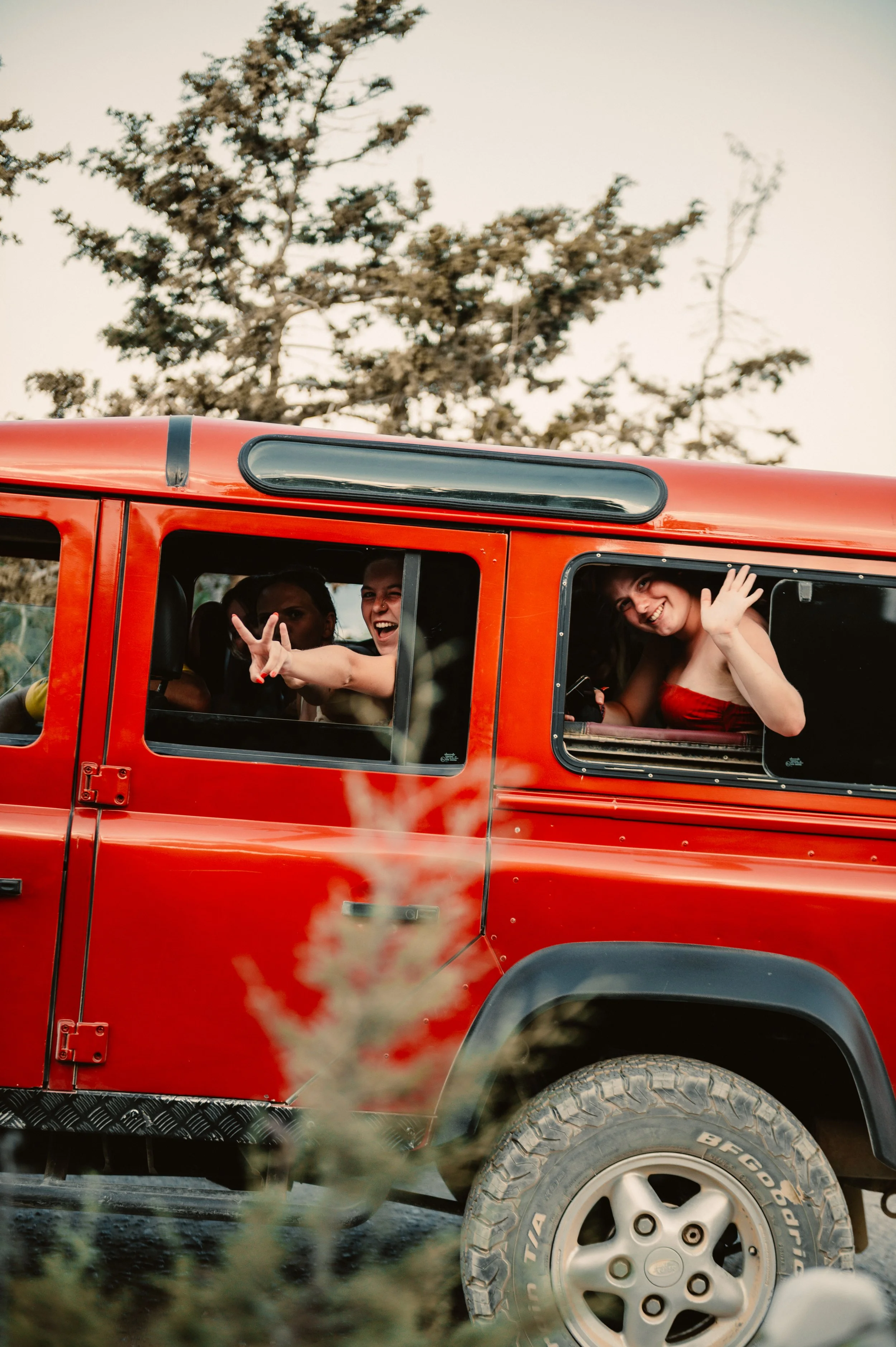 Red SUV with people smiling and waving from the windows, trees in the background.