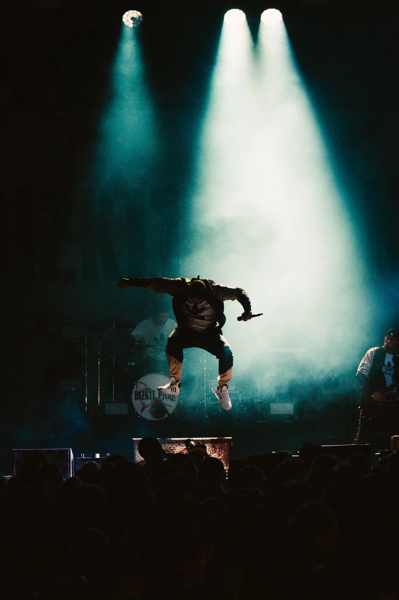 Musician jumping on stage during a live concert, with spotlight and smoke effects, crowd watching
