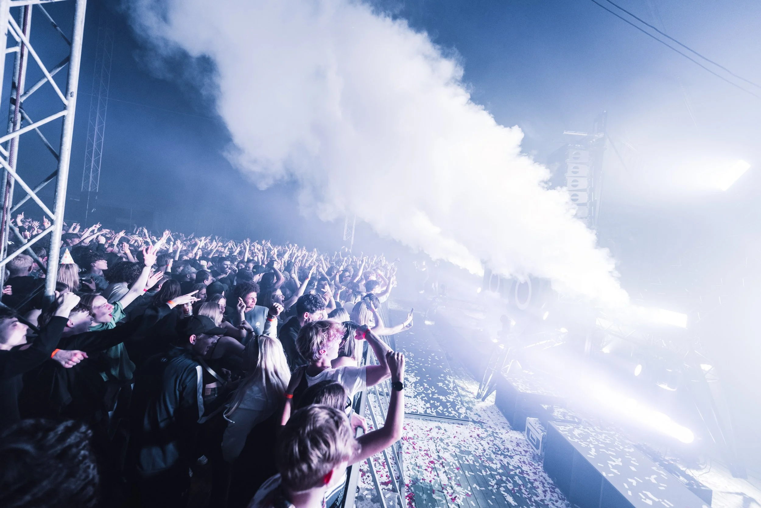 Crowd at a concert with stage lights and smoke effects.