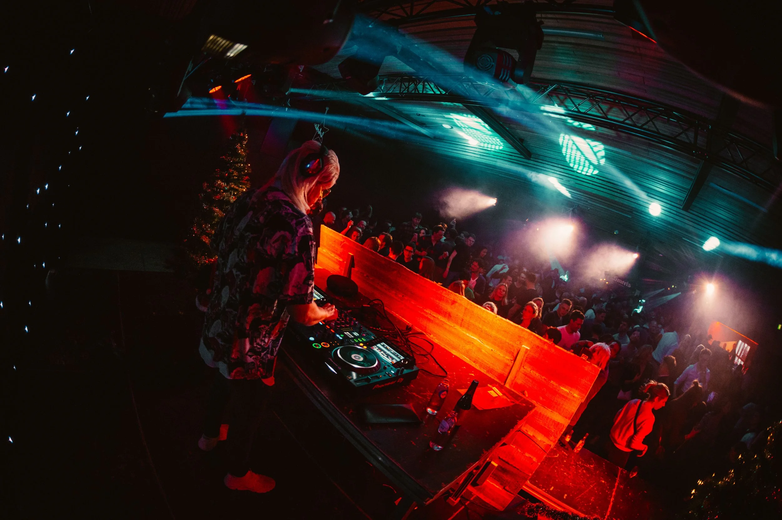 DJ performing at a crowded nightclub with colorful lights and a lively audience.