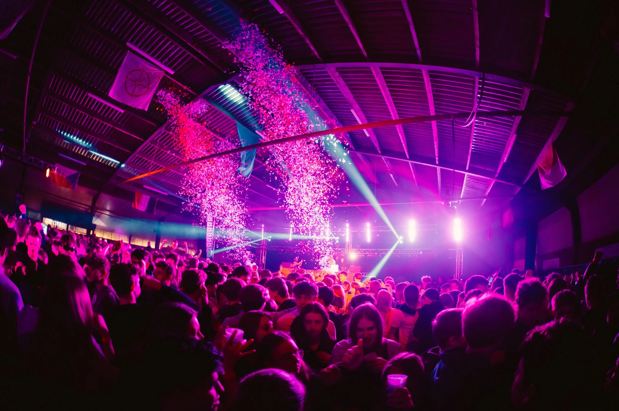 Crowded indoor concert with bright stage lights and confetti falling