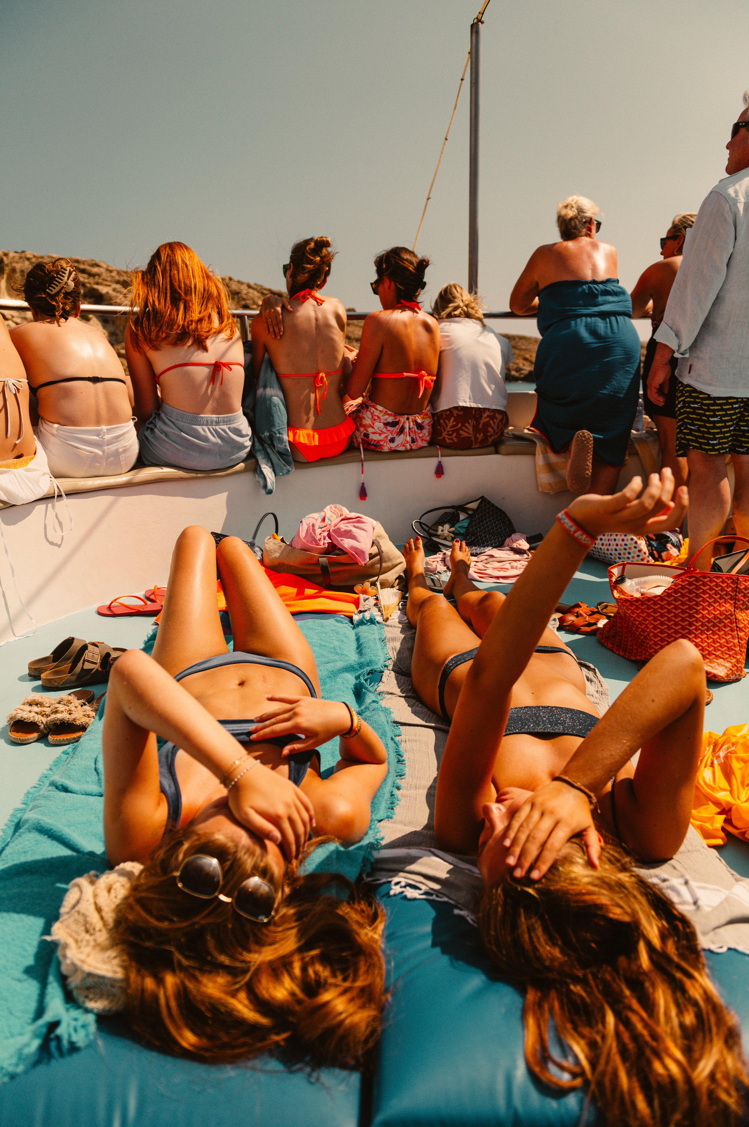 People in swimsuits lounging and sitting on a boat under sunny weather.