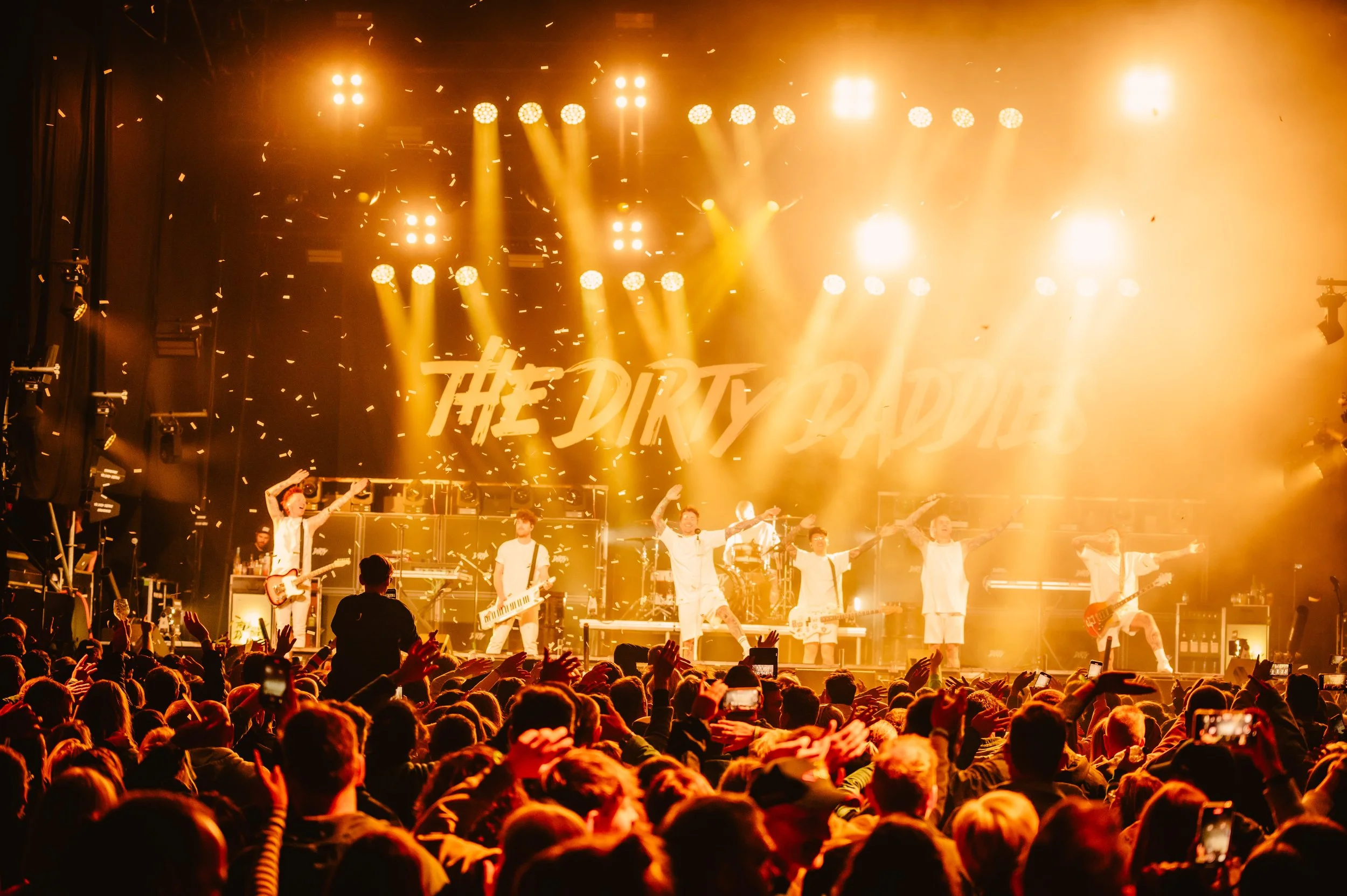 Live band performance on stage with bright lights and enthusiastic audience.