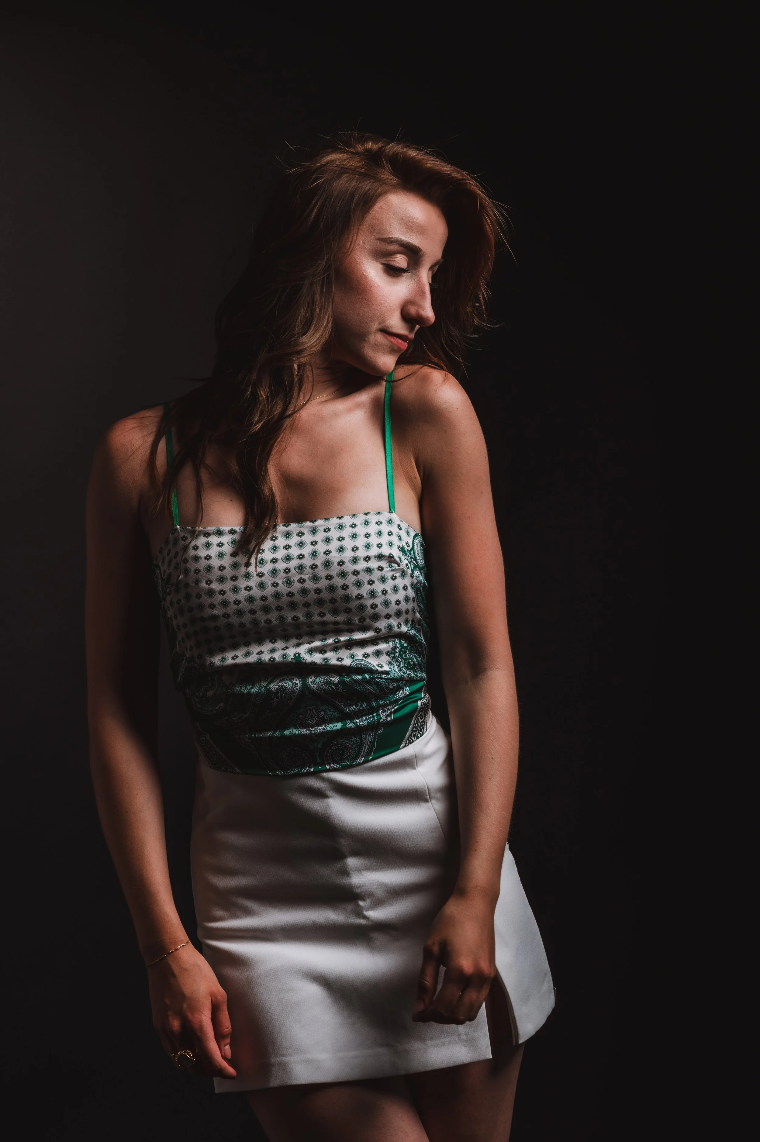 Woman in patterned top and white skirt posing against dark background