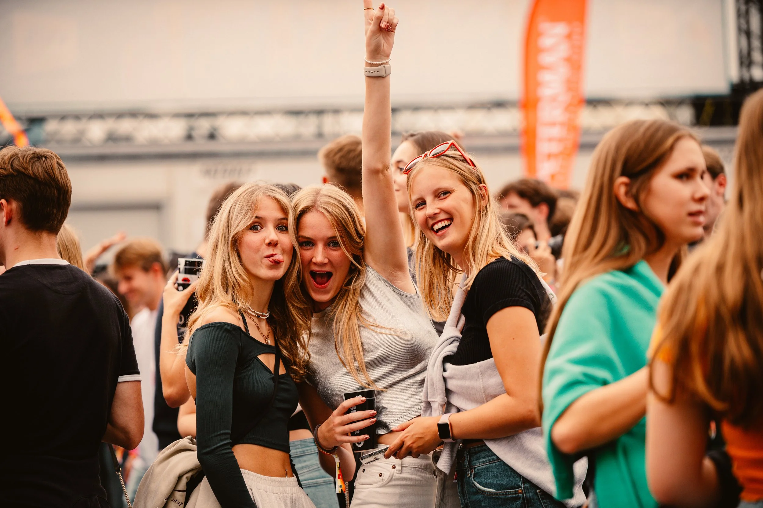 Three young women enjoying a lively outdoor event, with one raising her arm in excitement and all three smiling at the camera.