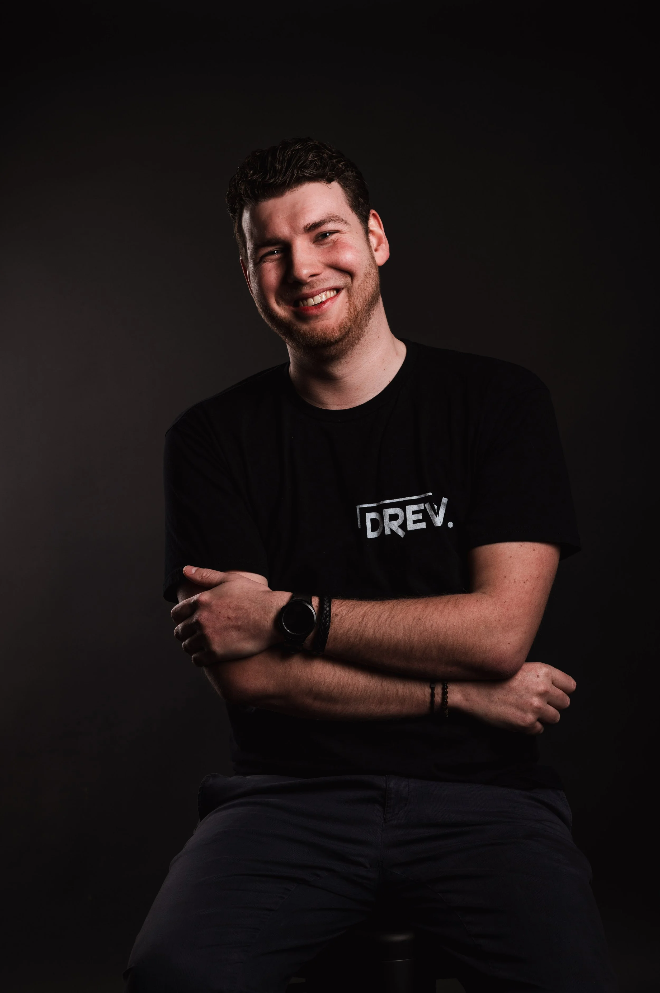 Smiling person in black t-shirt with "DREV" logo, posing against a dark background.