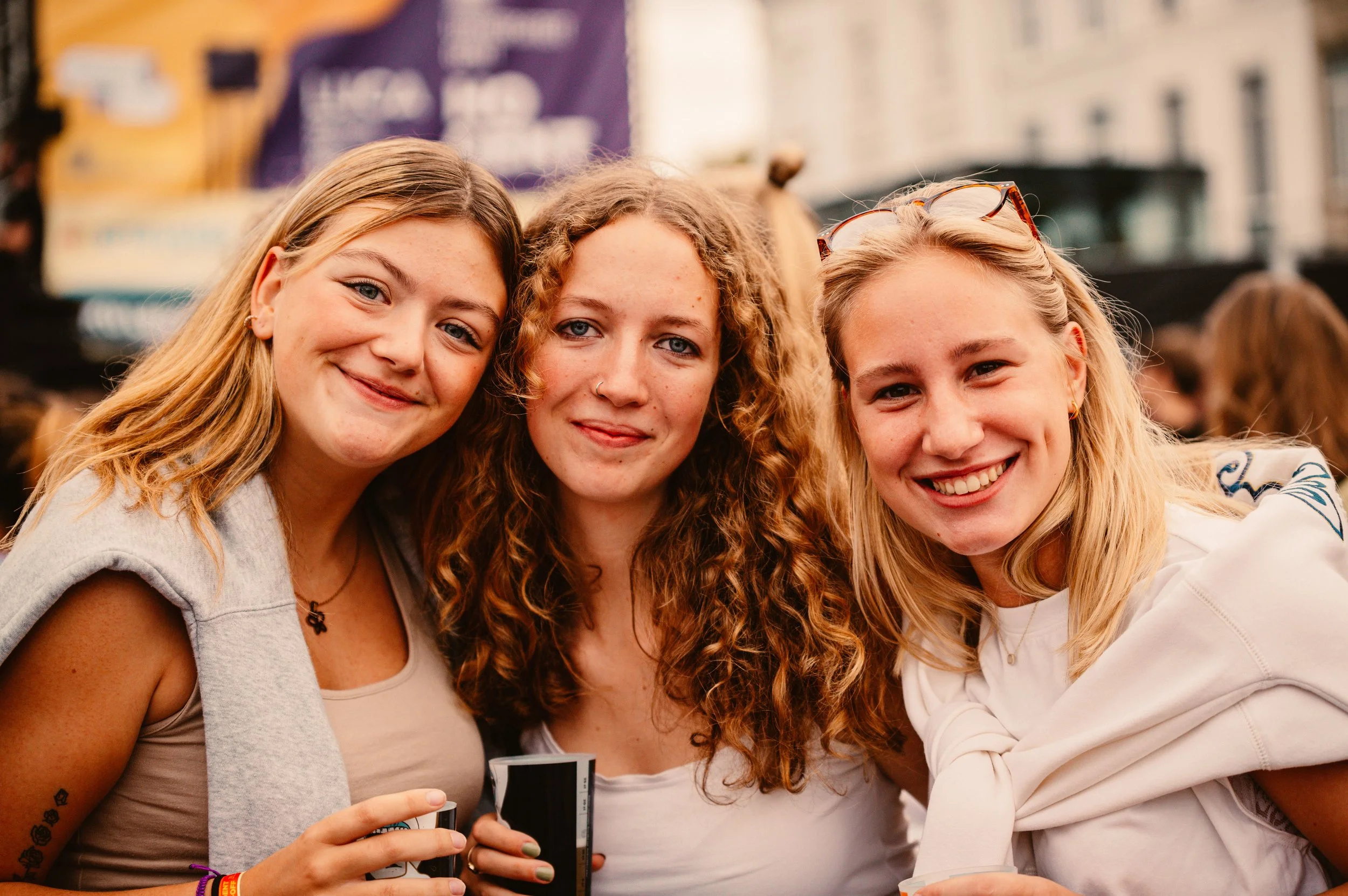 Three smiling young women posing together at an outdoor event.
