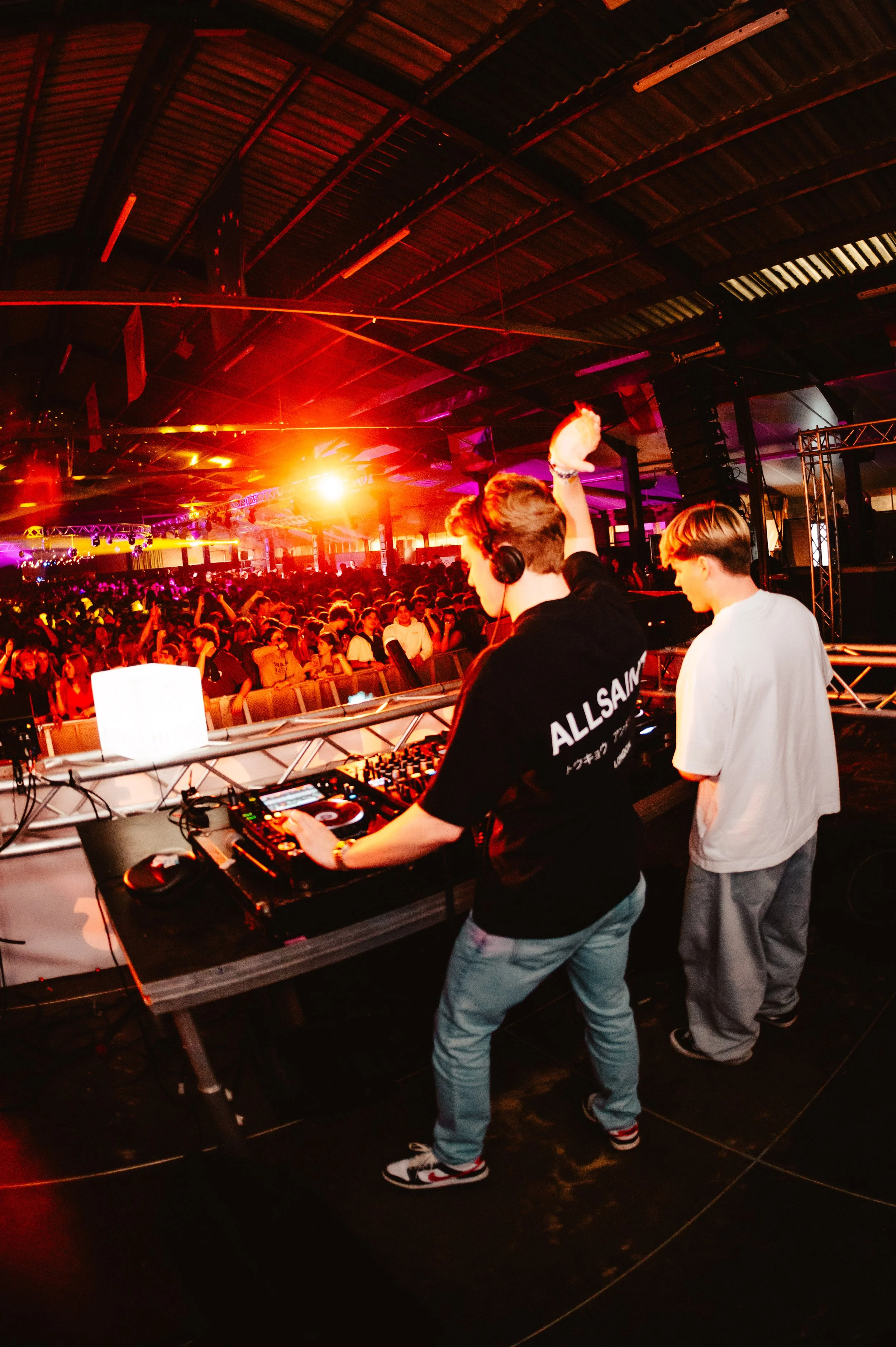 DJ performing at a nightclub with a large crowd, colorful lighting and a vibrant atmosphere.