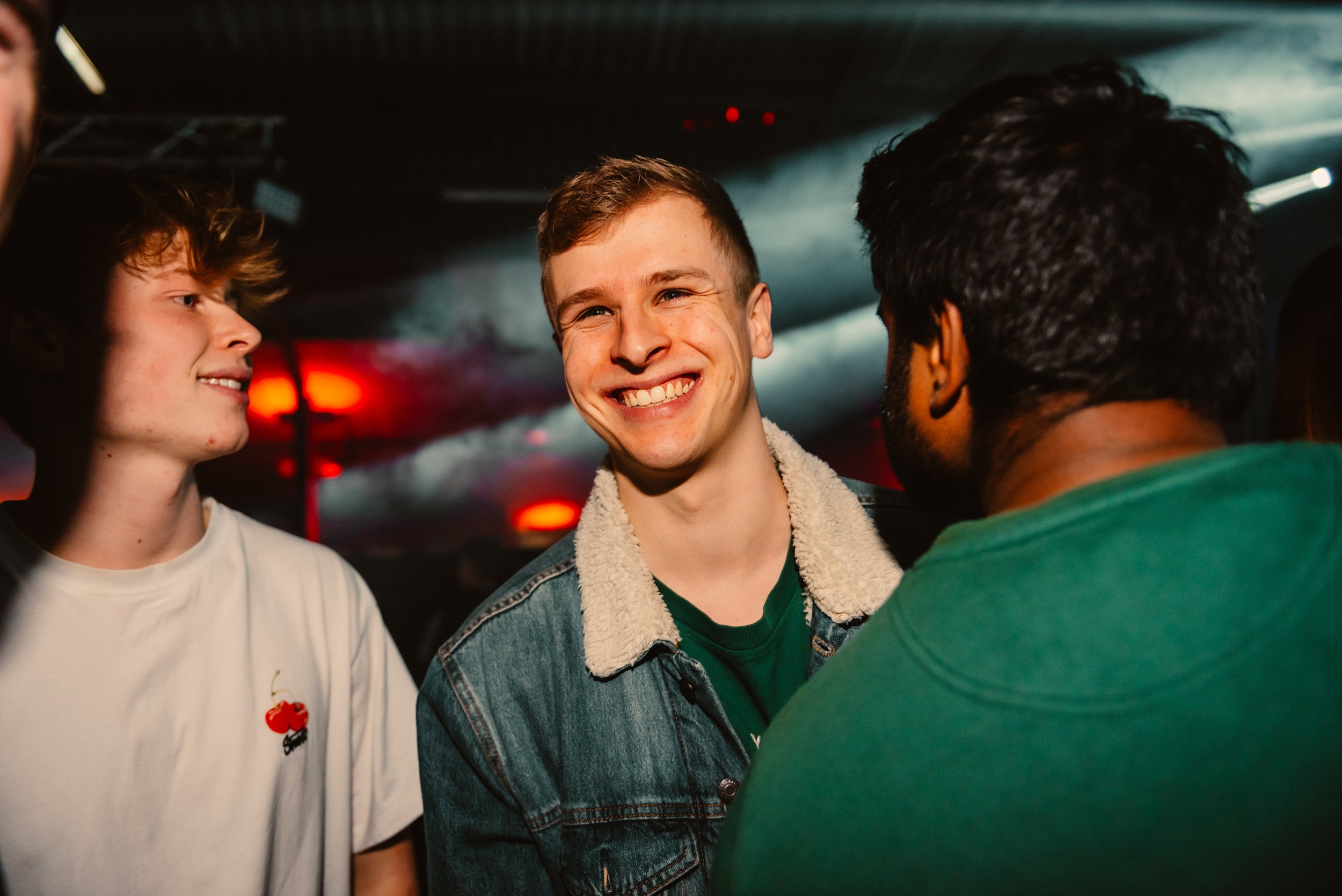 Group of young people smiling and talking in a club with red and blue lights.