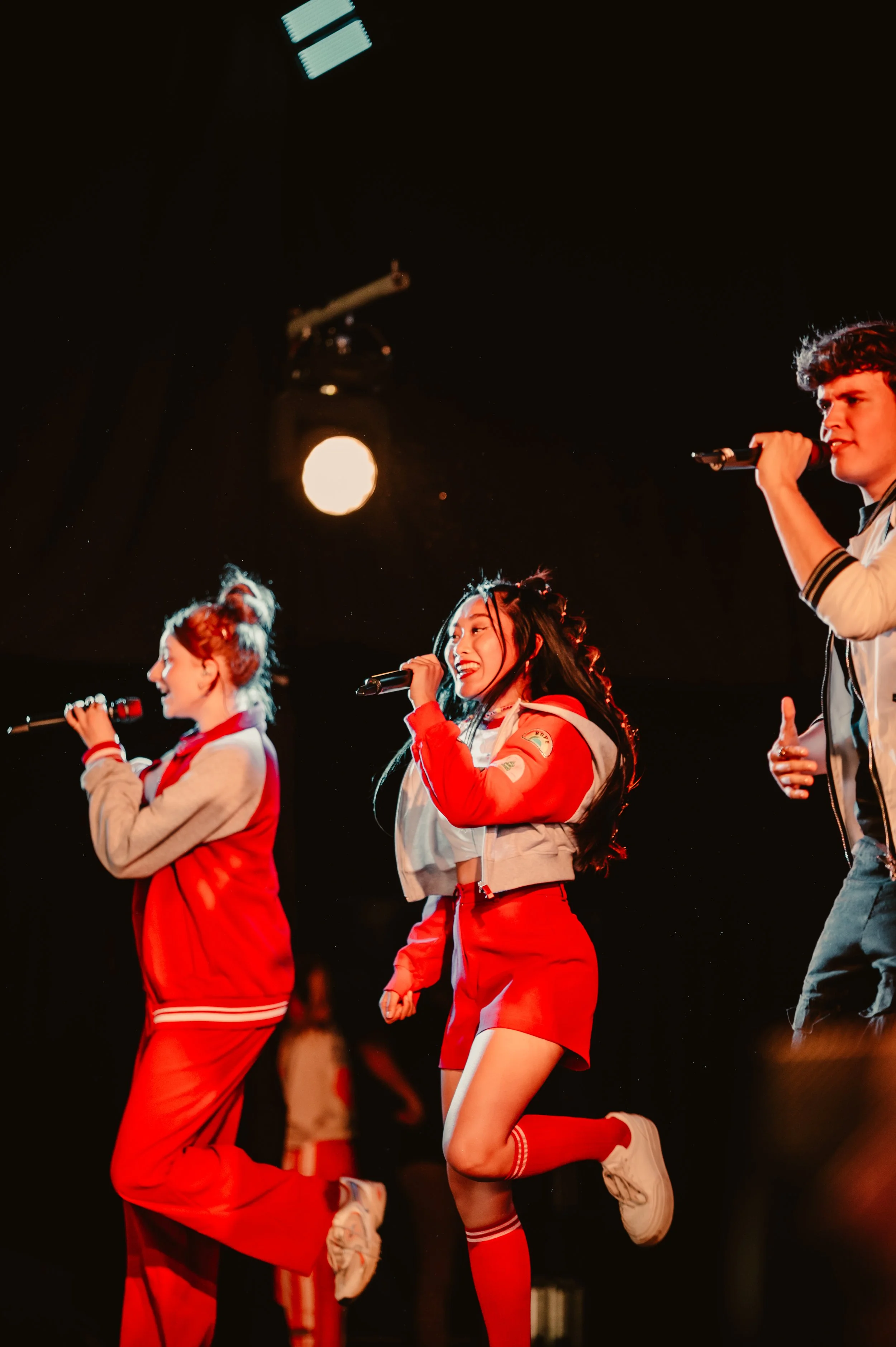 Group of performers singing on stage with microphones, wearing colorful costumes, spotlights illuminating them.