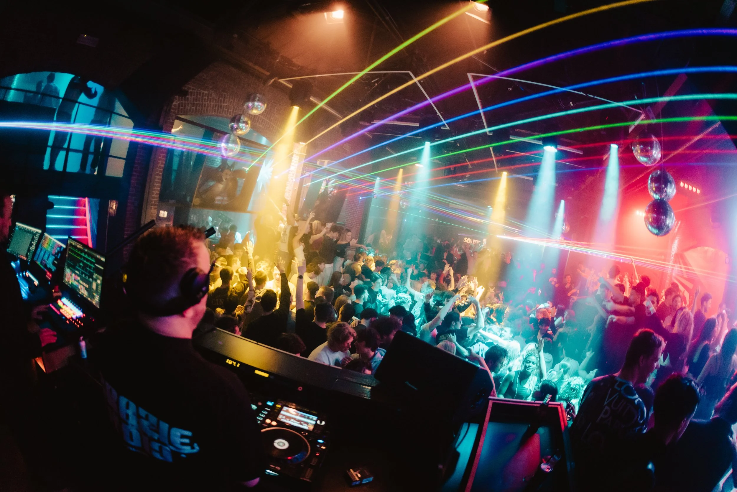 Crowded nightclub with DJ, colorful lights, and dancing people