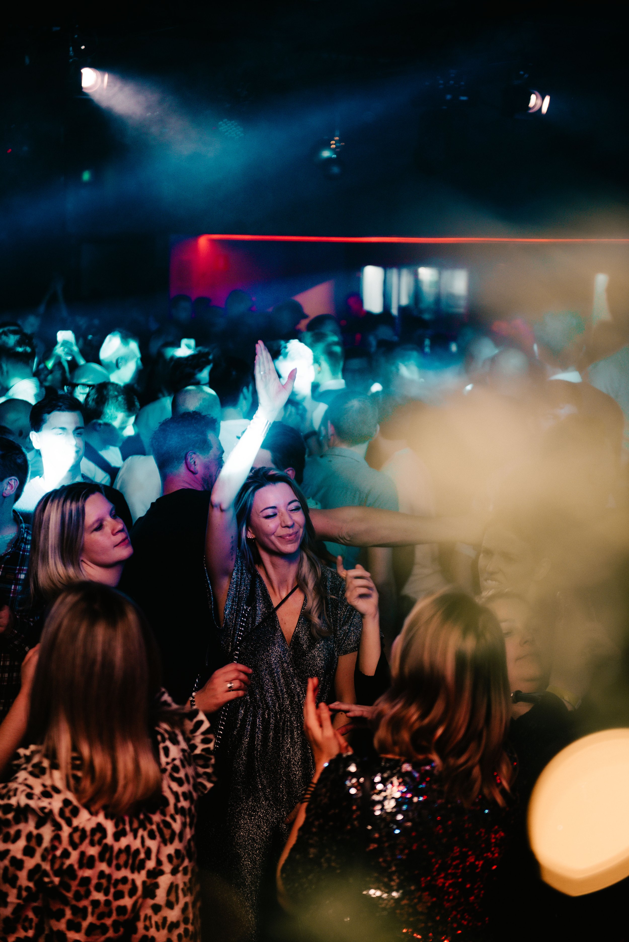 Crowded nightclub scene with people dancing, colorful lights and a party atmosphere.