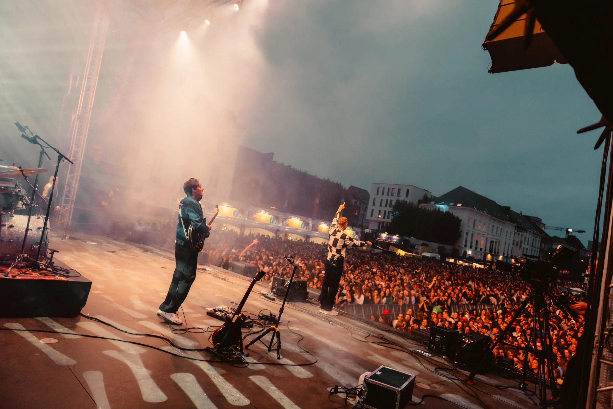 Performers on stage during an outdoor concert with a large crowd and stage lights.