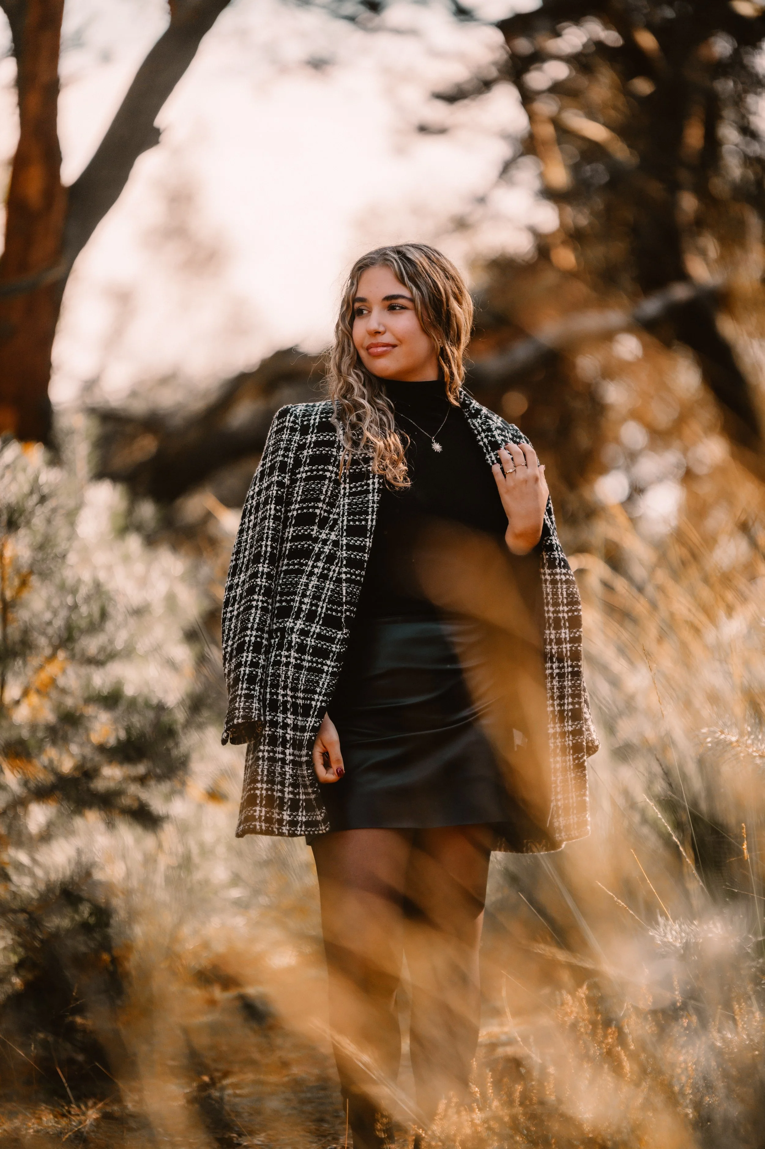 Woman in black and white checkered coat standing outdoors with nature background