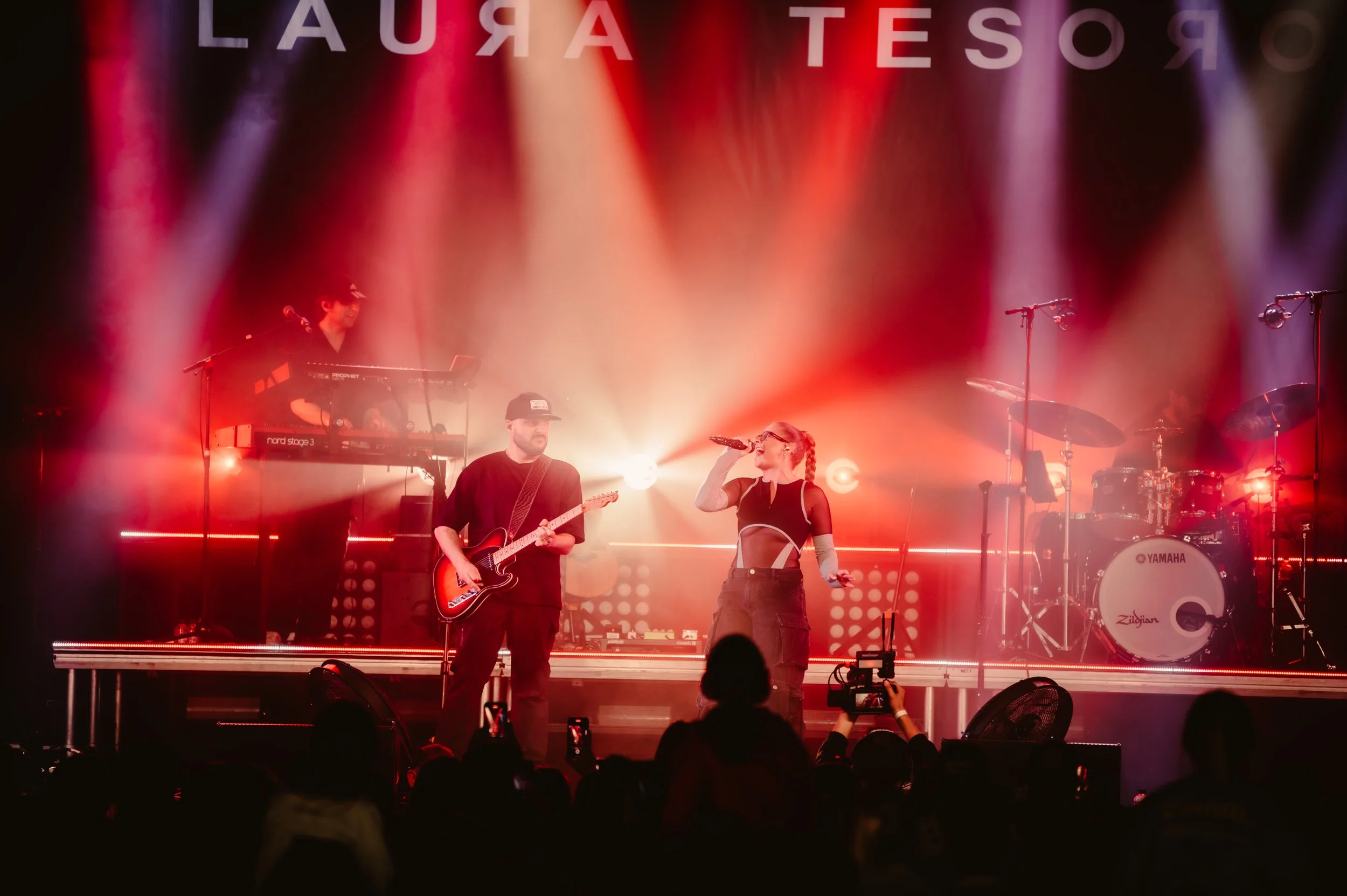 Musical performance on stage with vibrant lighting, featuring a singer, guitarist, keyboardist, and drummer.