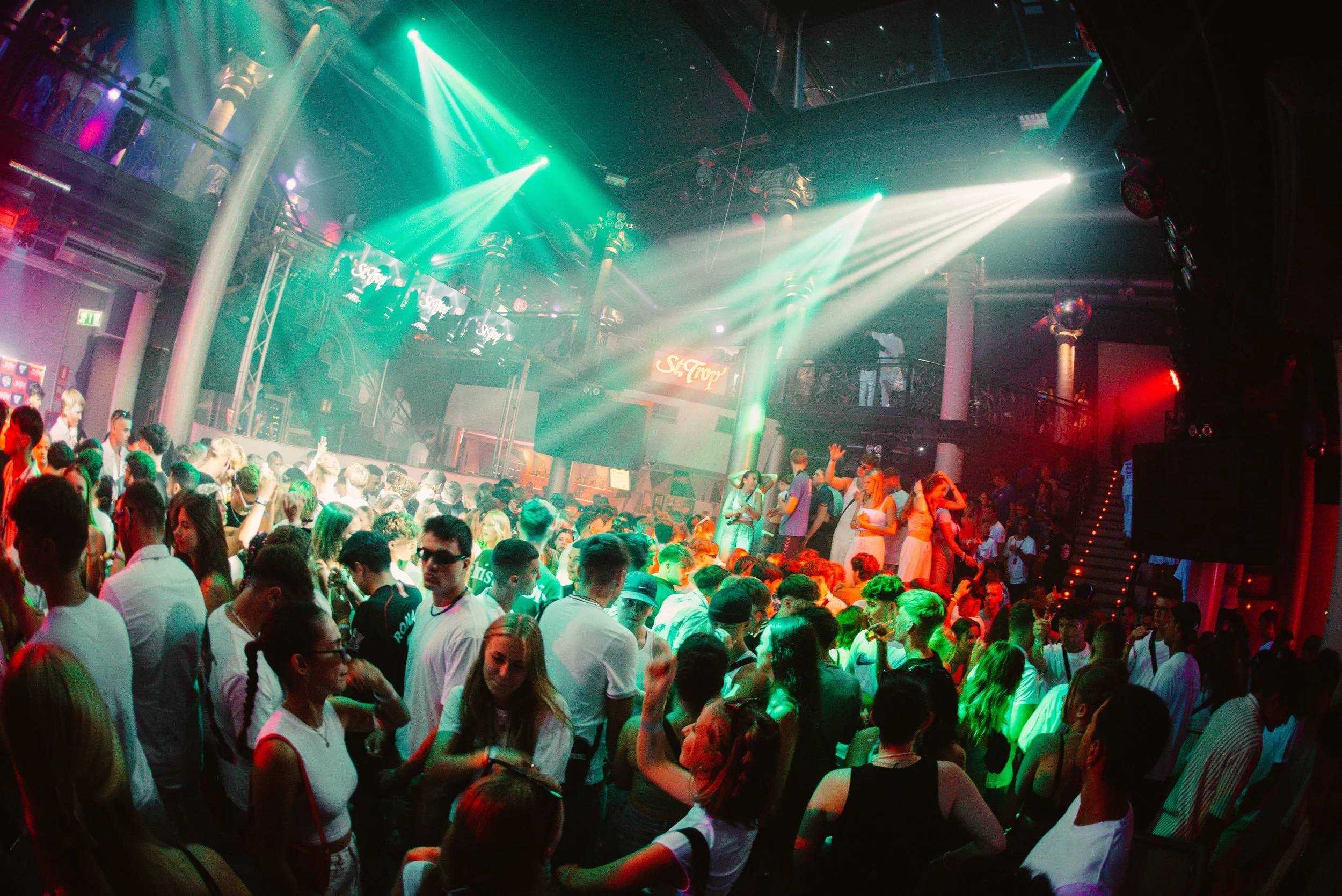 Crowded nightclub with people dancing under colorful lights.