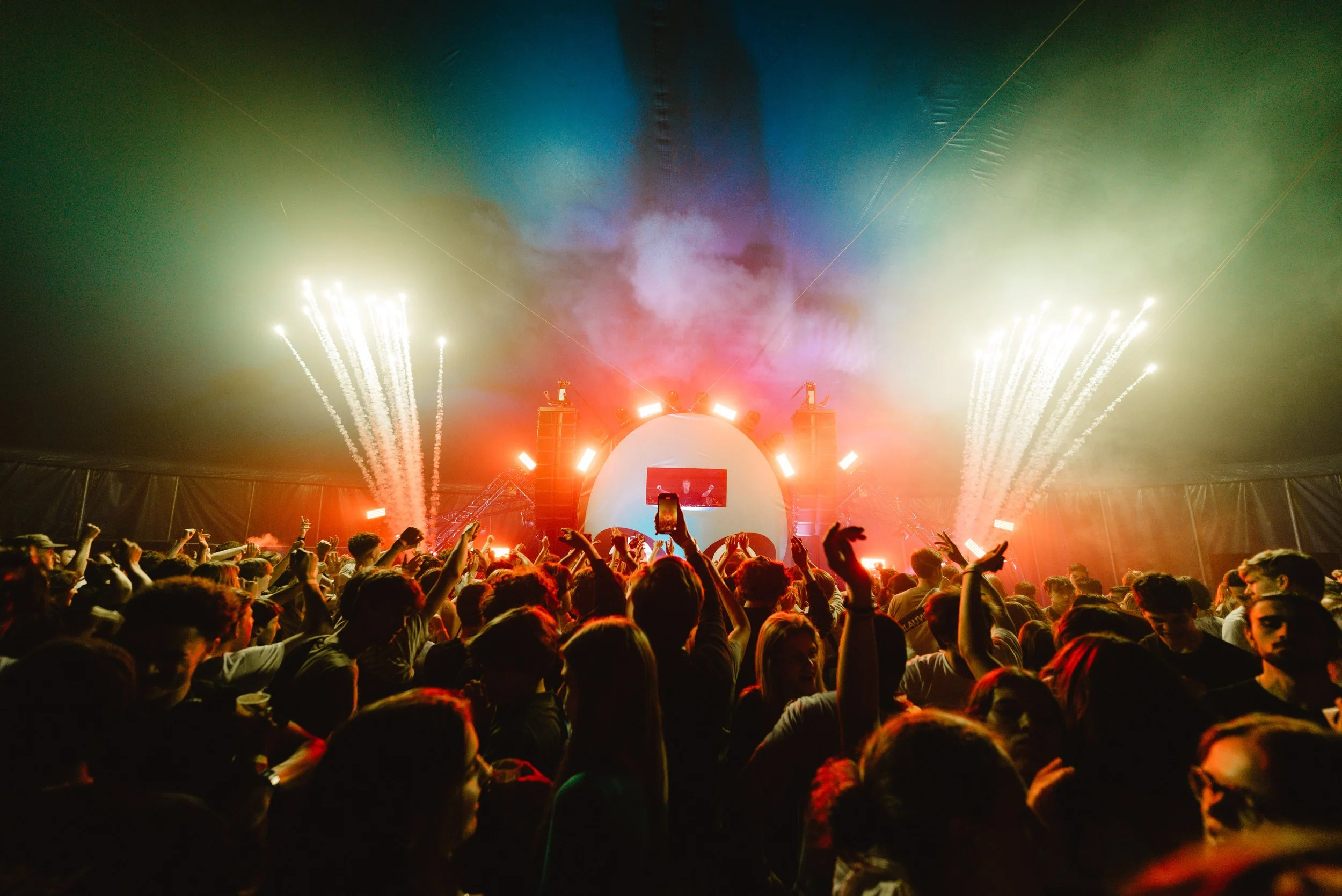 Crowd enjoying a concert with a colorful light show and fireworks.