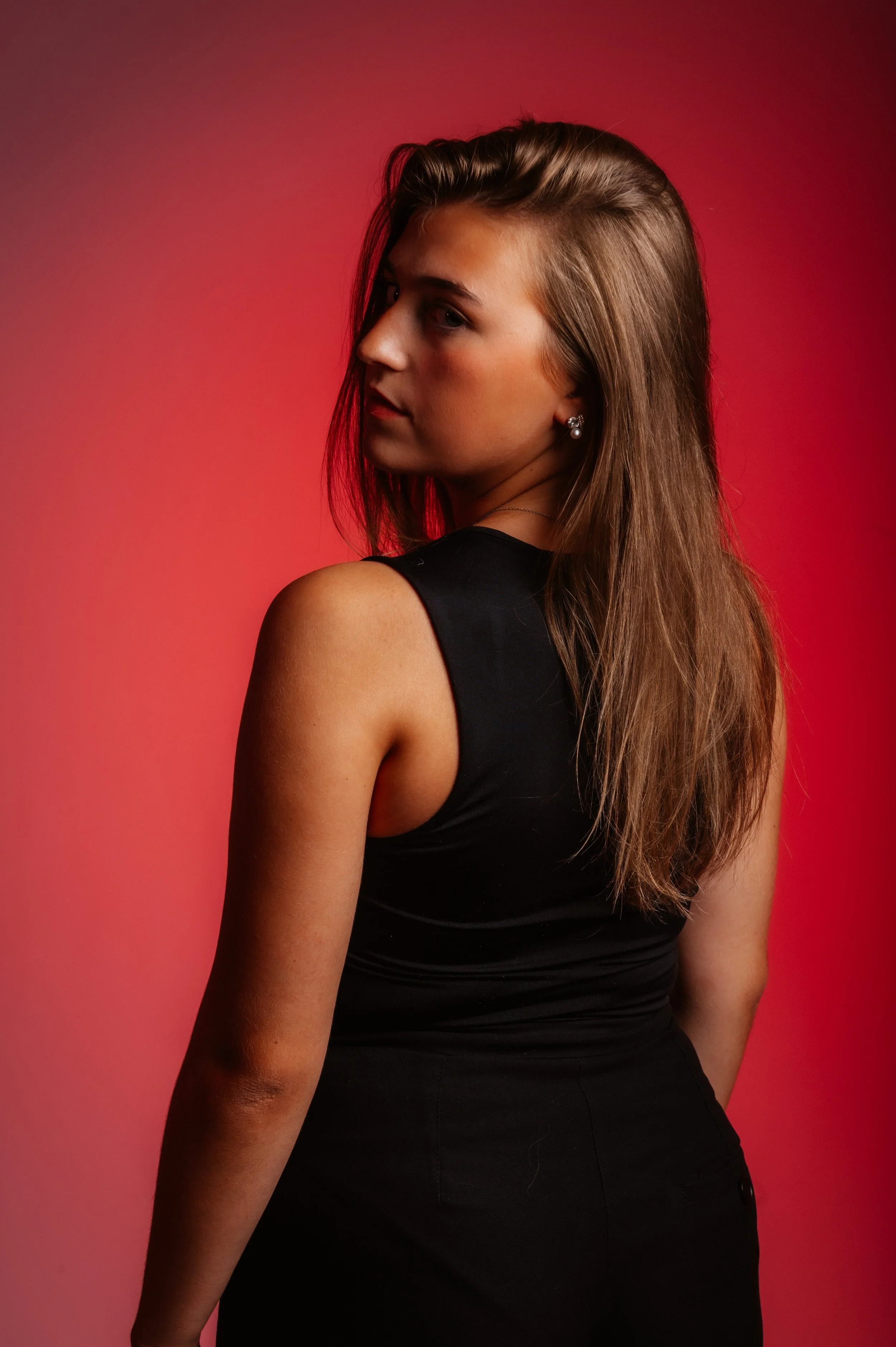 Woman in black sleeveless top posing against a red background