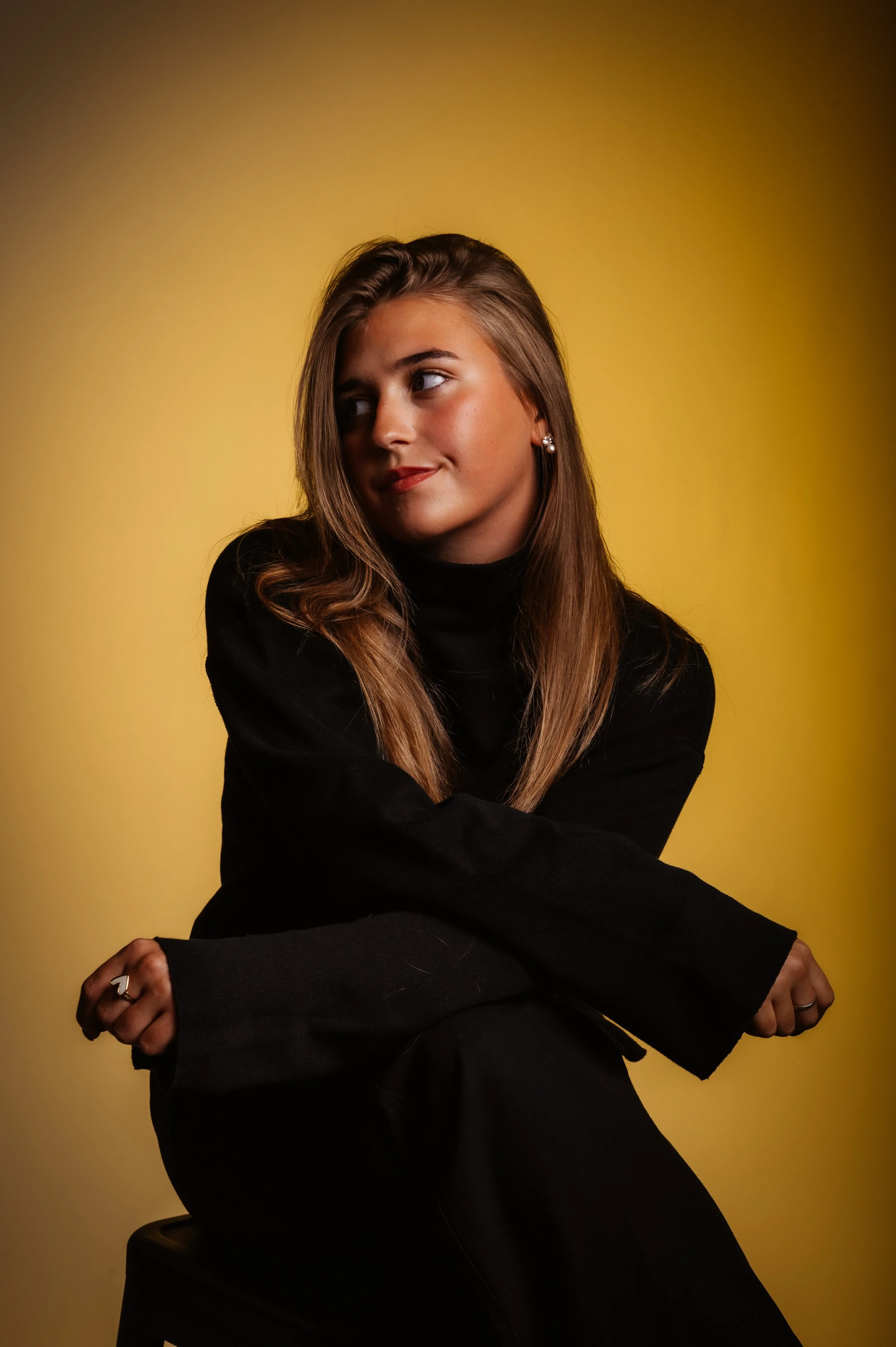 Woman in black sweater posing against a yellow background.