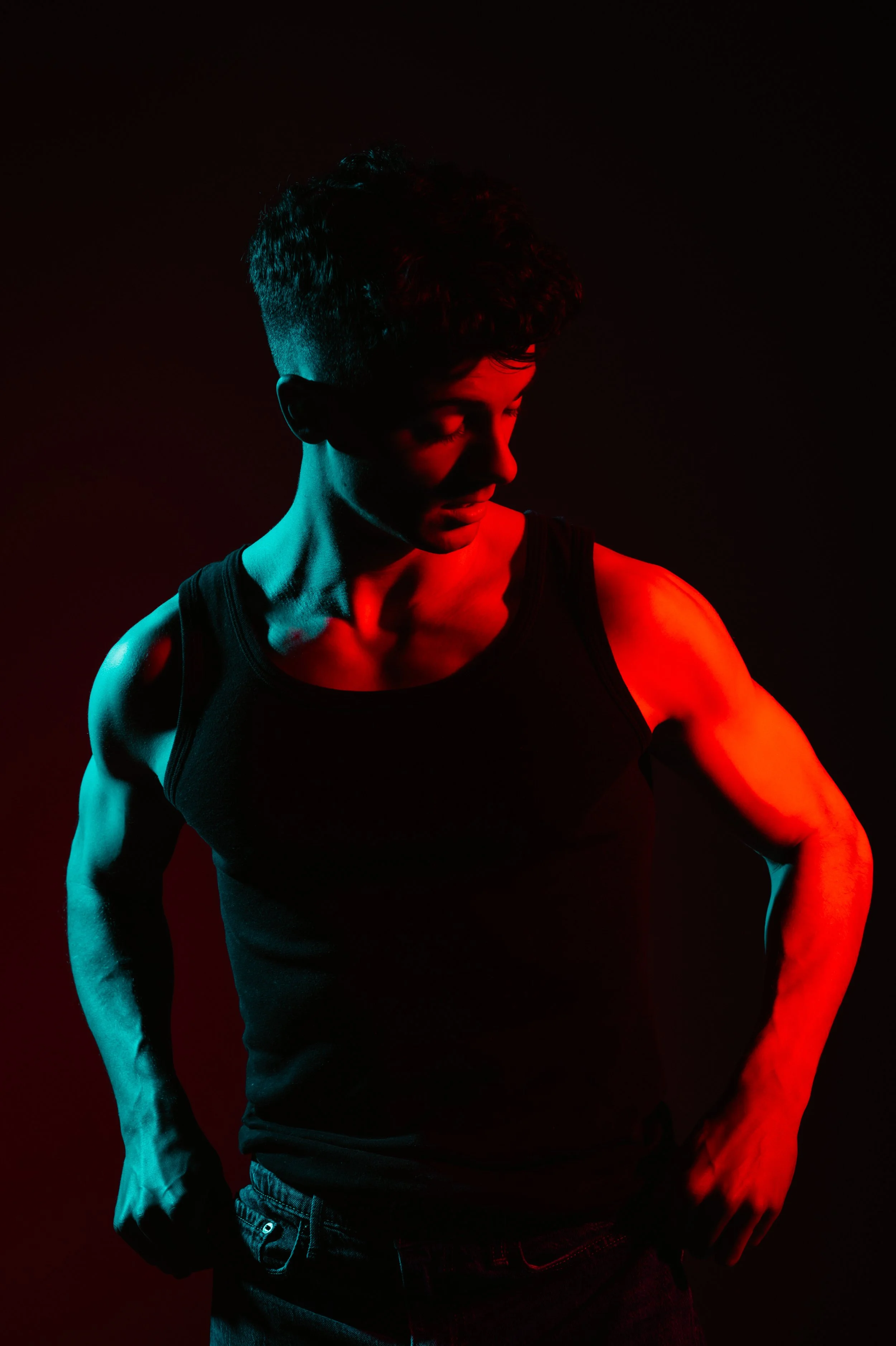 Man wearing a black tank top illuminated by red and blue lighting, posing in shadows.