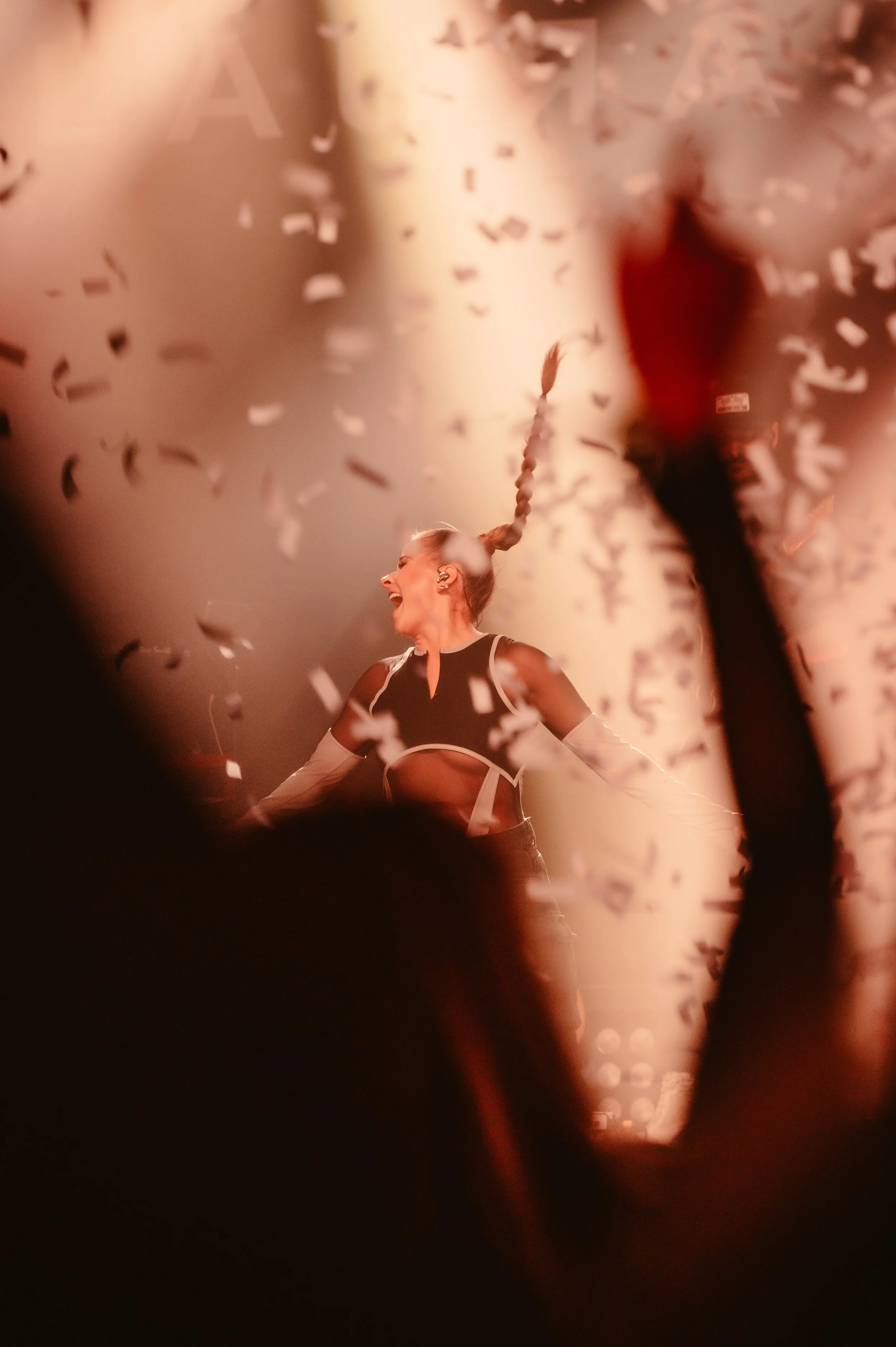 Performer on stage with confetti falling, vibrant lighting, and crowd silhouette.
