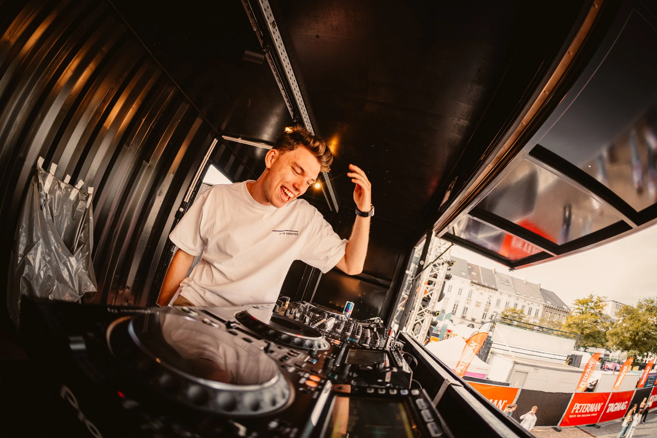 DJ performing in a booth with turntables in an outdoor event setting.