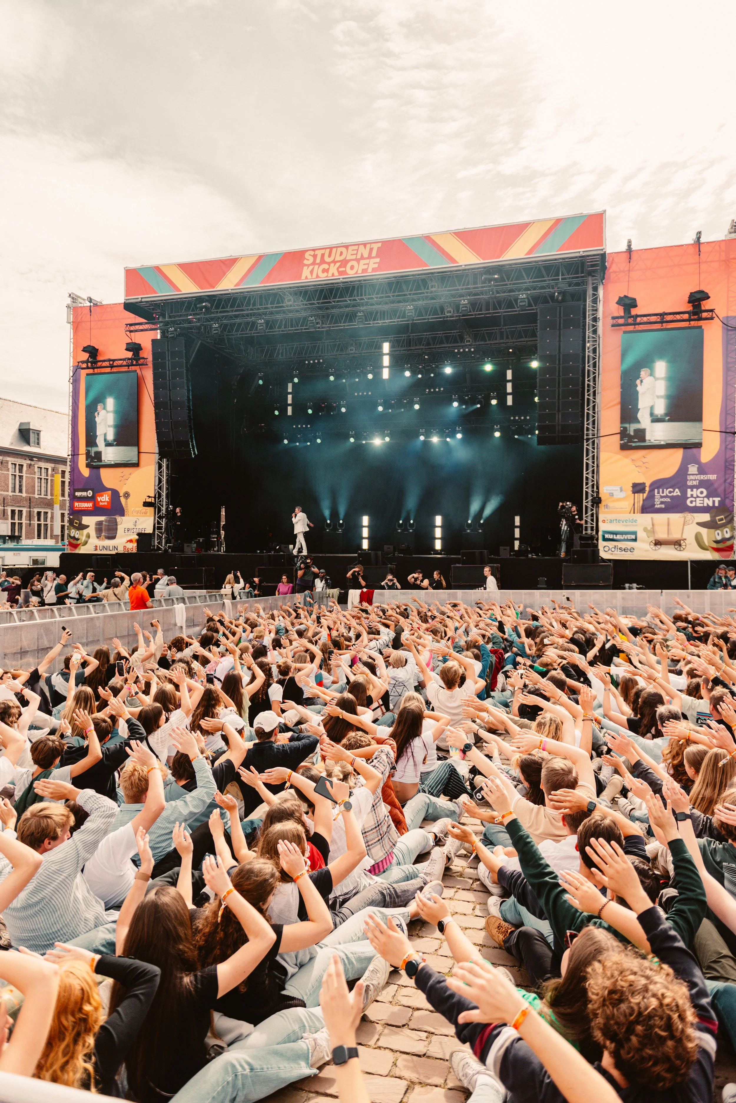 Crowd of students at outdoor concert during "Student Kick-off" event, with raised hands facing a large stage.