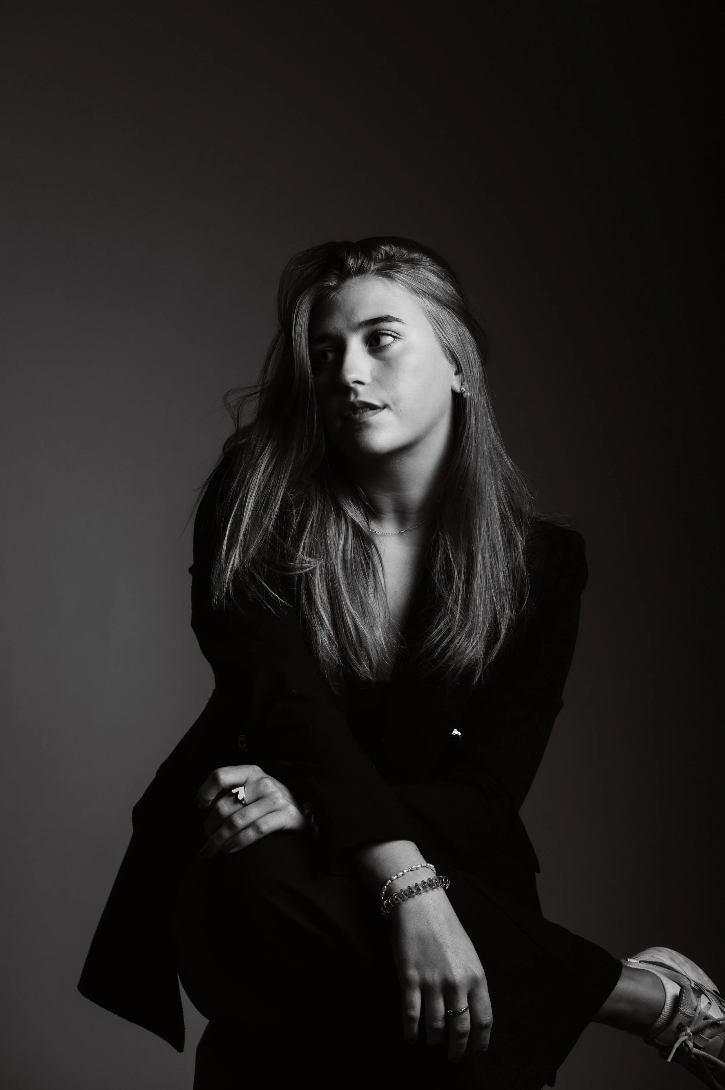 Black and white portrait of a woman with long hair, wearing a dark outfit, sitting and looking to the side.