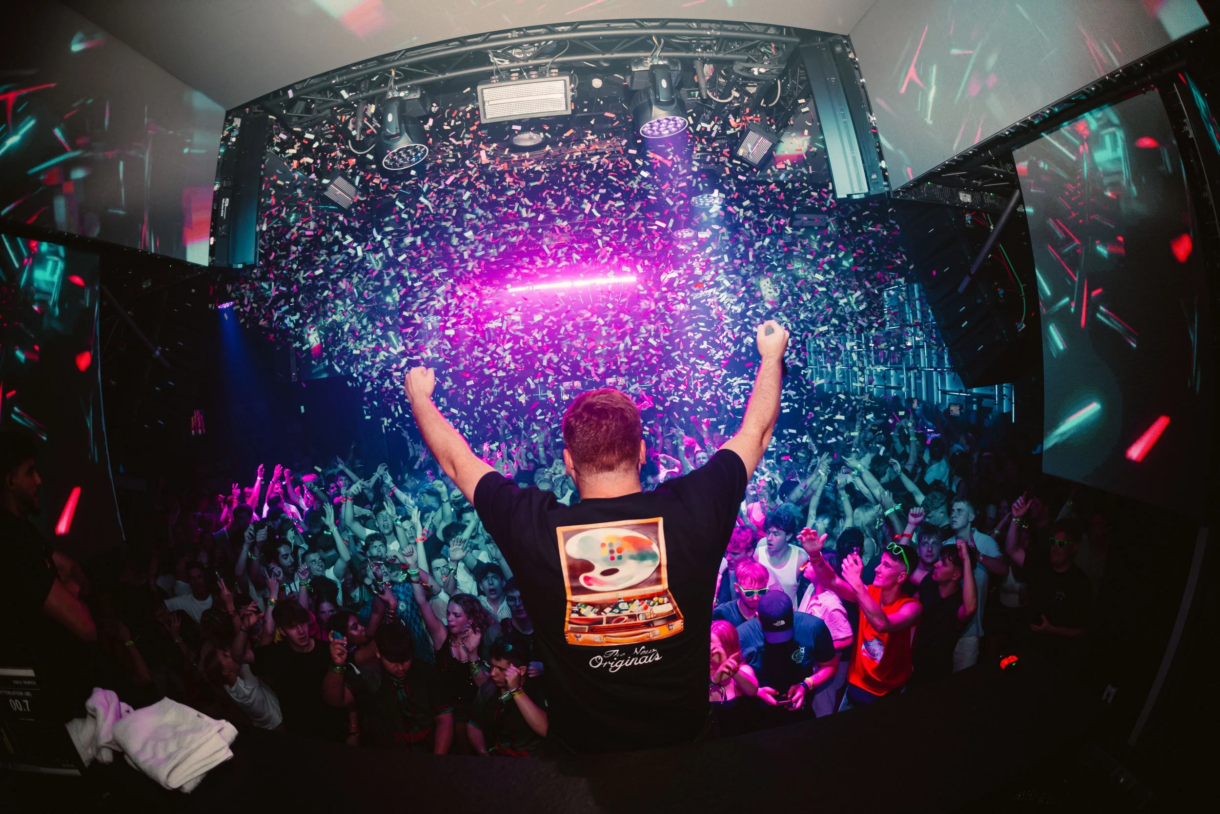 DJ facing audience at a concert with crowd cheering and colorful confetti falling