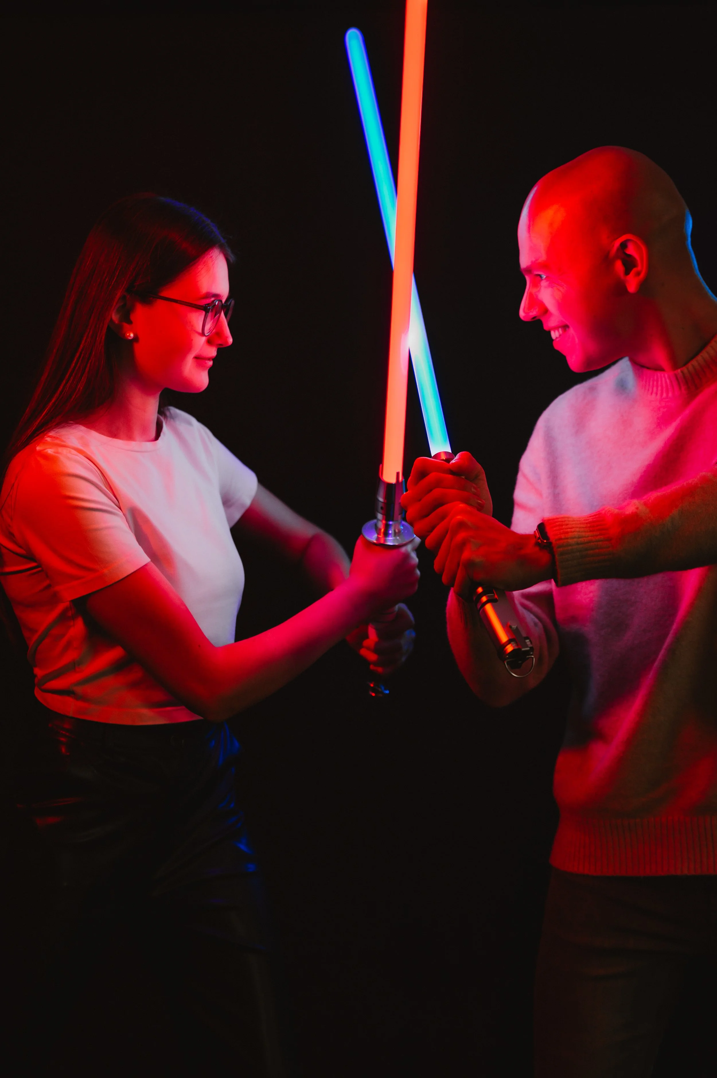 Two people having fun with lightsabers, one holding a blue lightsaber and the other a red lightsaber, with a dark background.