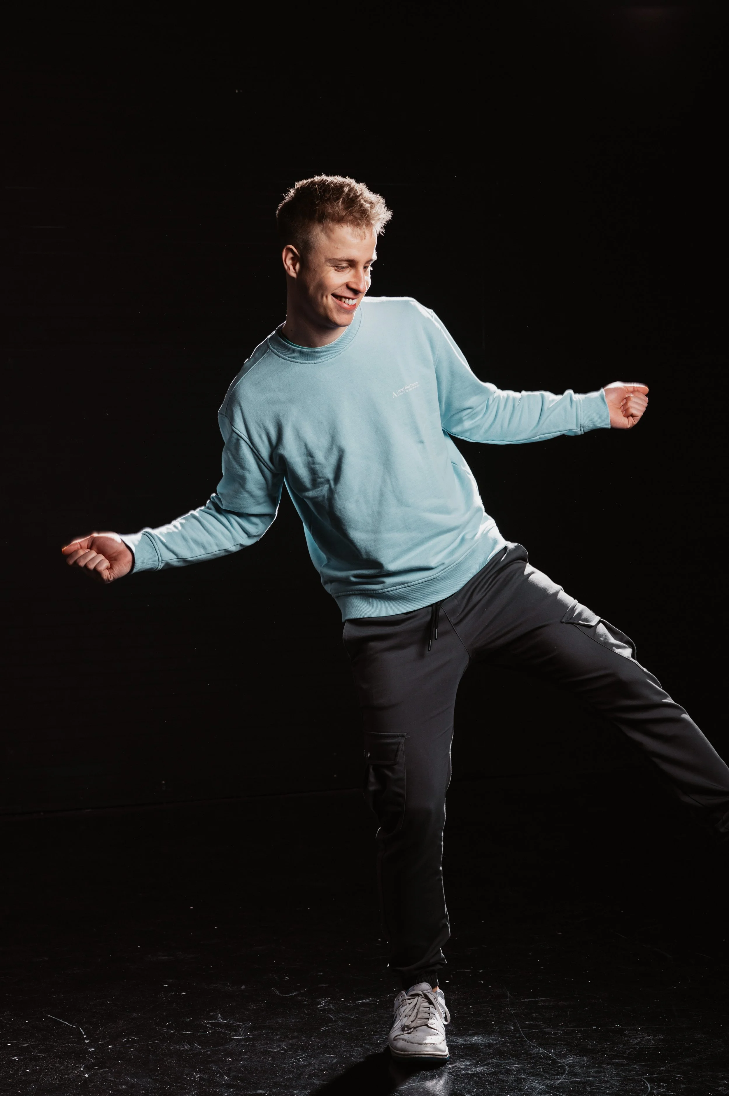 Man dancing in a studio, wearing a light blue sweatshirt and black pants.
